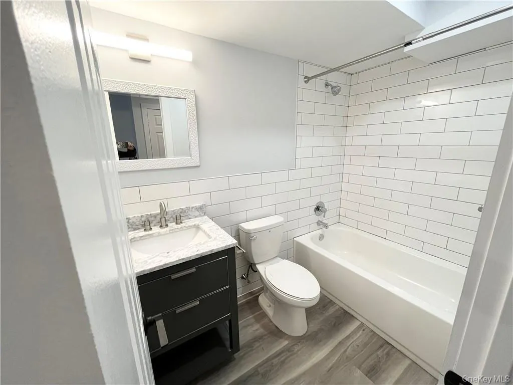 Full bath featuring vanity, tile walls, bathing tub / shower combination, and dark wood finished floors Full bath featuring vanity, tile walls, bathing tub / shower combination, and dark wood finished floors