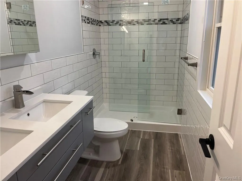 Bathroom featuring double vanity, tile walls, a shower stall, and dark wood finished floors Bathroom featuring double vanity, tile walls, a shower stall, and dark wood finished floors