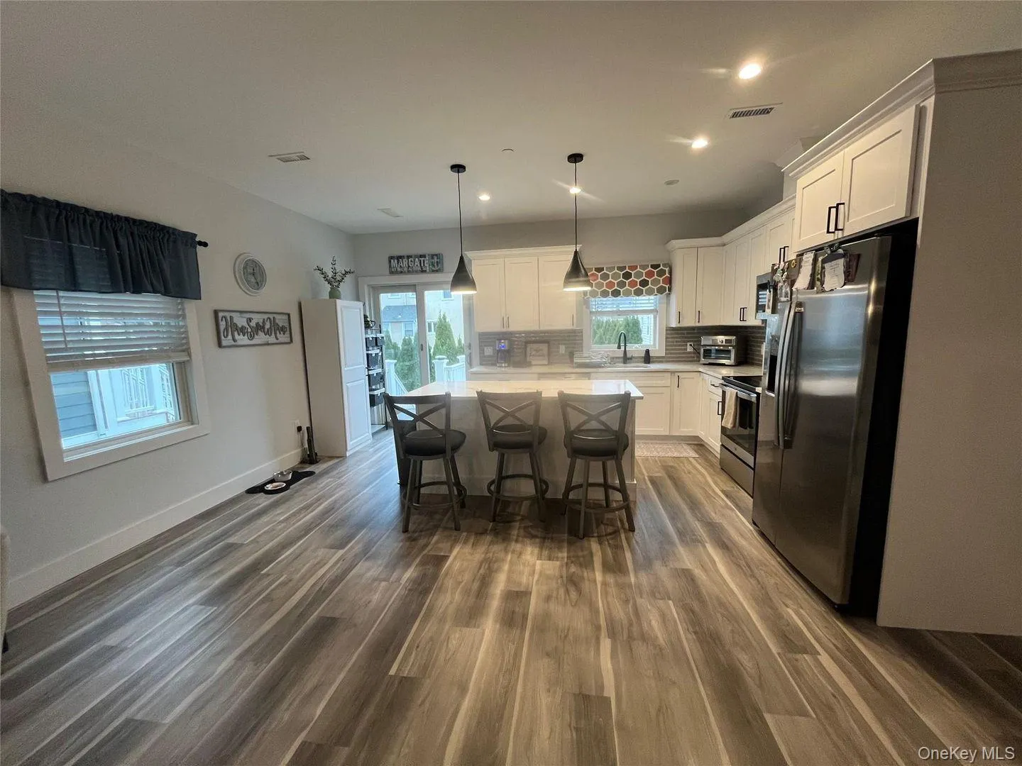 Kitchen with appliances with stainless steel finishes, white cabinetry, a kitchen island, dark wood-style flooring, and recessed lighting Kitchen with appliances with stainless steel finishes, white cabinetry, a kitchen island, dark wood-style flooring, and recessed lighting