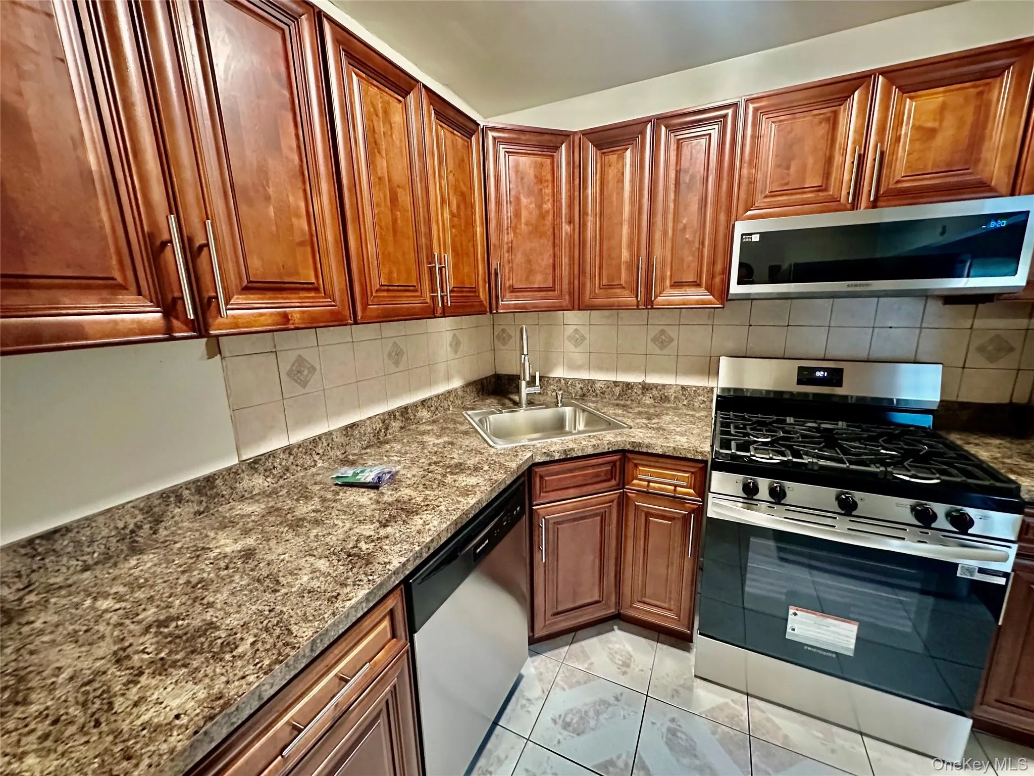 Kitchen with appliances with stainless steel finishes, brown cabinetry, dark stone countertops, and decorative backsplash Kitchen with appliances with stainless steel finishes, brown cabinetry, dark stone countertops, and decorative backsplash
