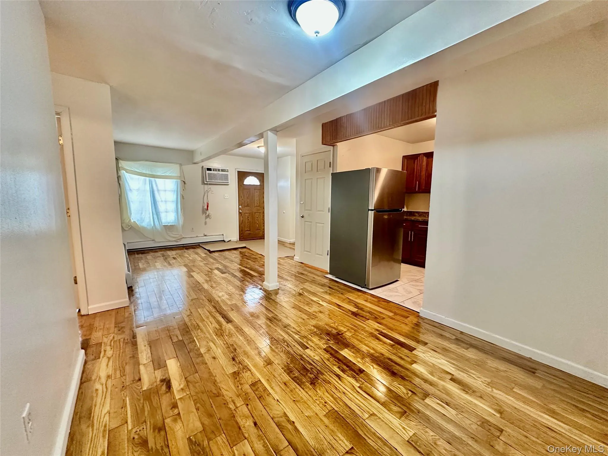 Unfurnished living room featuring light wood-type flooring, baseboard heating, and a wall mounted AC Unfurnished living room featuring light wood-type flooring, baseboard heating, and a wall mounted AC