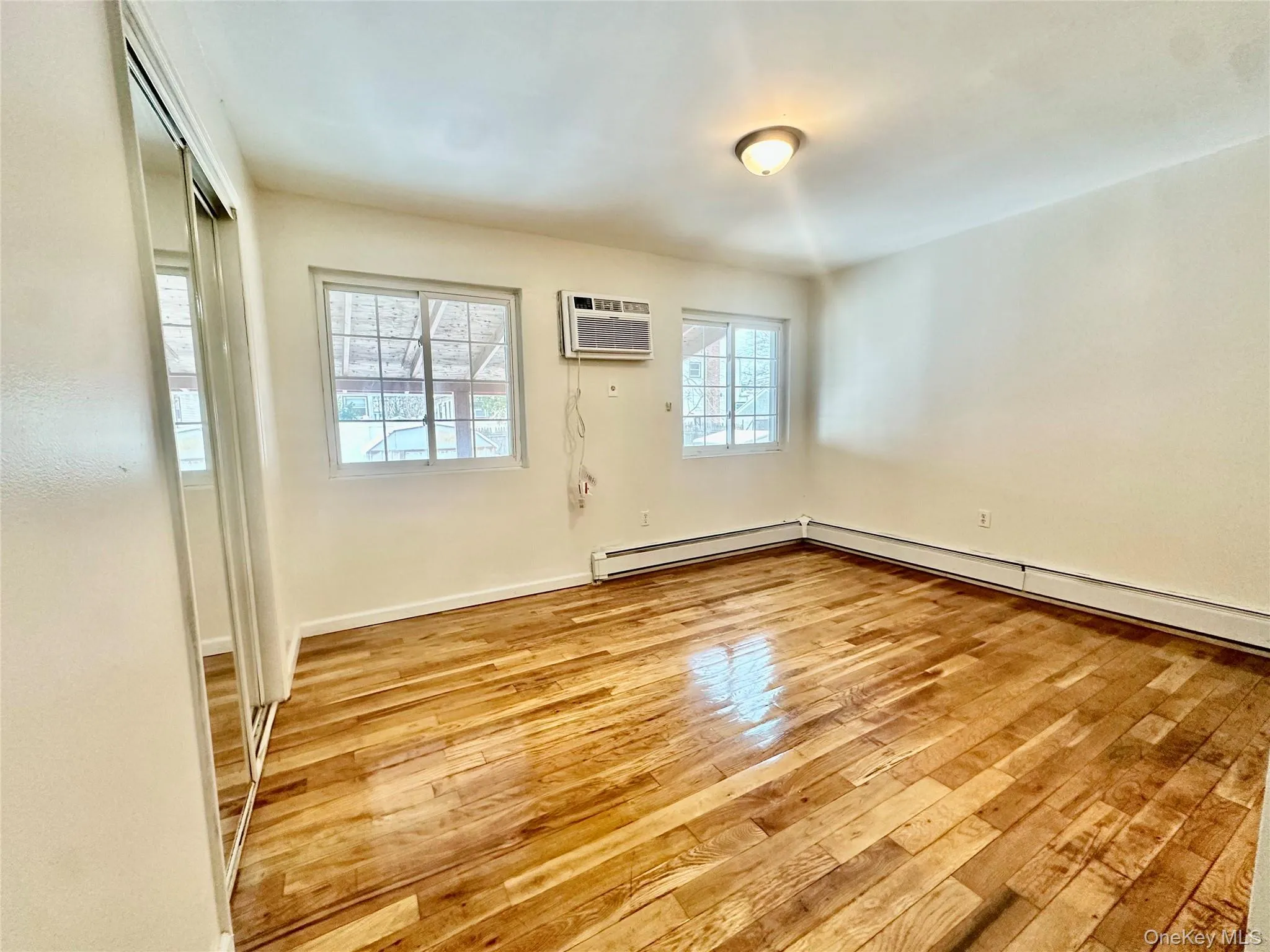 Empty room with light wood-style flooring and an AC wall unit Empty room with light wood-style flooring and an AC wall unit