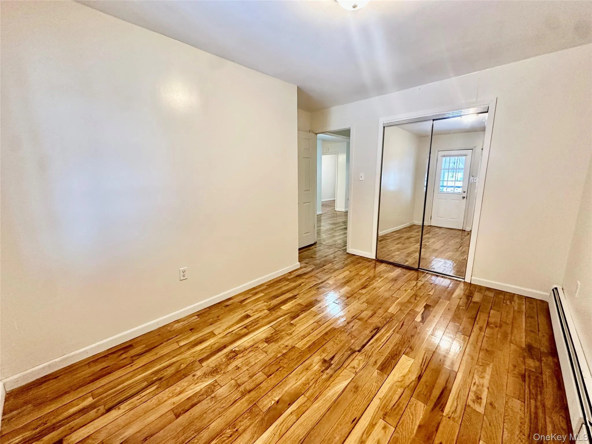Unfurnished bedroom with a baseboard radiator, light wood finished floors, and a closet Unfurnished bedroom with a baseboard radiator, light wood finished floors, and a closet