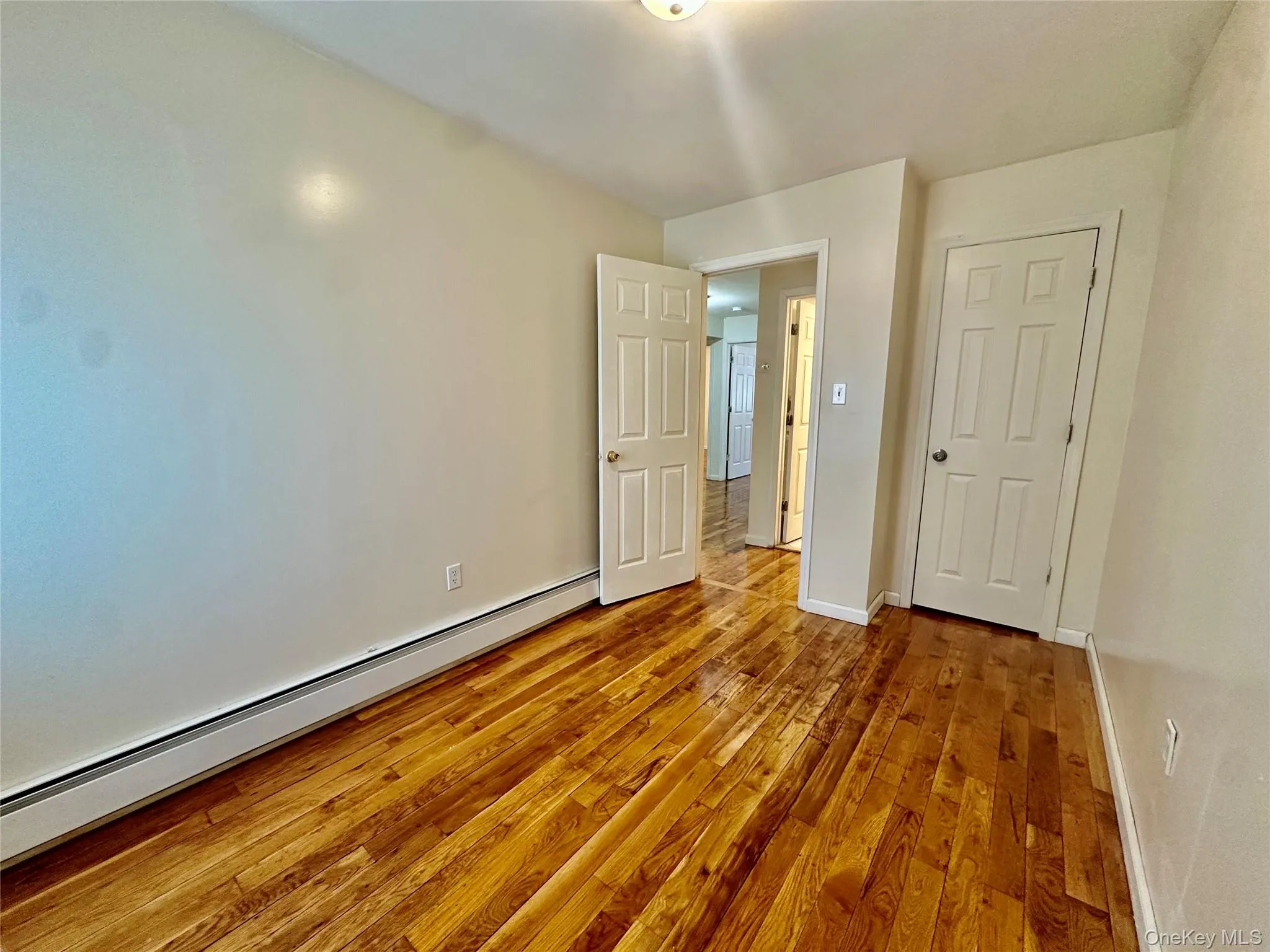 Unfurnished bedroom featuring baseboard heating and light wood-style flooring Unfurnished bedroom featuring baseboard heating and light wood-style flooring