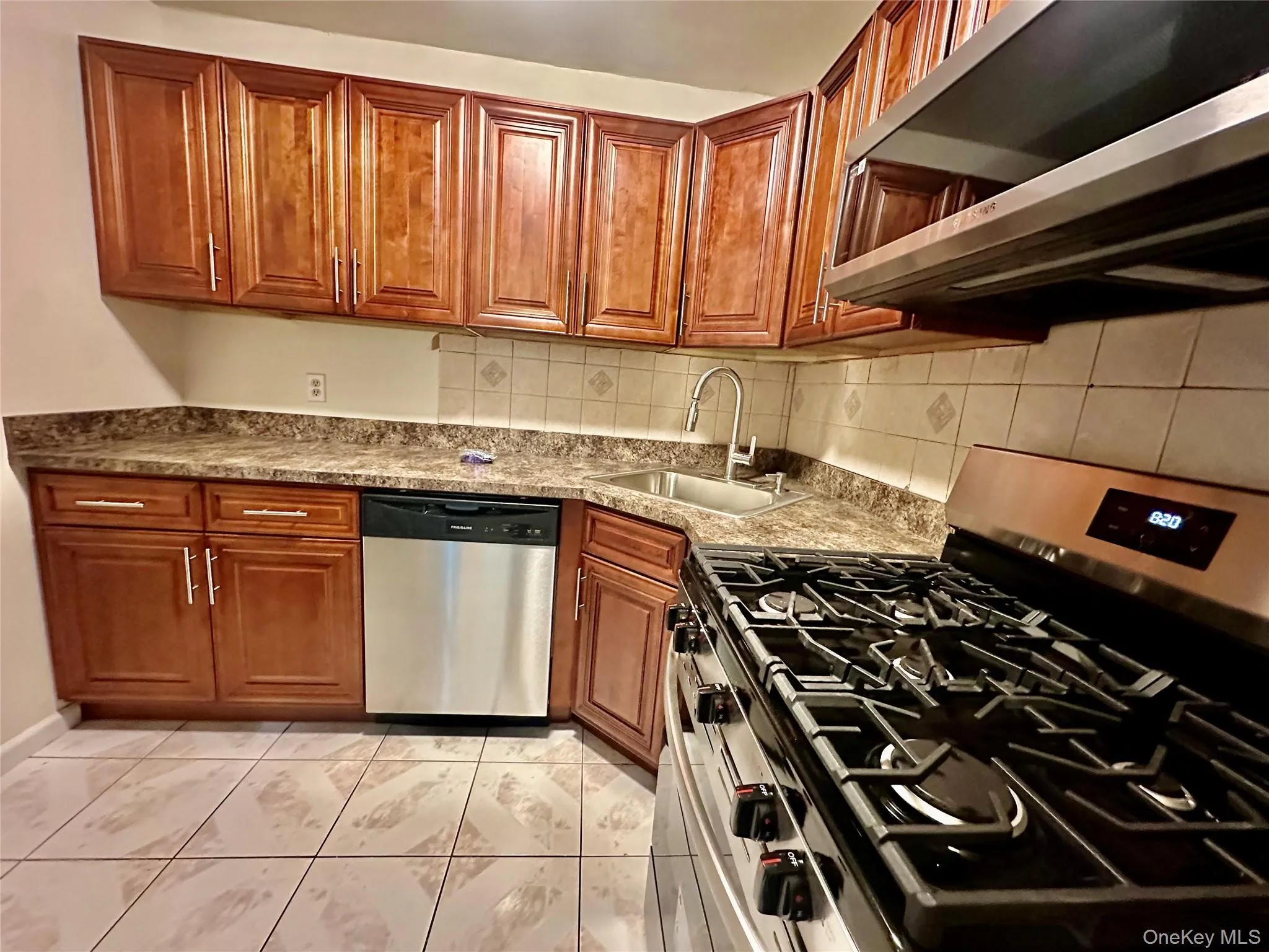 Kitchen with stainless steel appliances, brown cabinetry, tasteful backsplash, and light stone countertops Kitchen with stainless steel appliances, brown cabinetry, tasteful backsplash, and light stone countertops