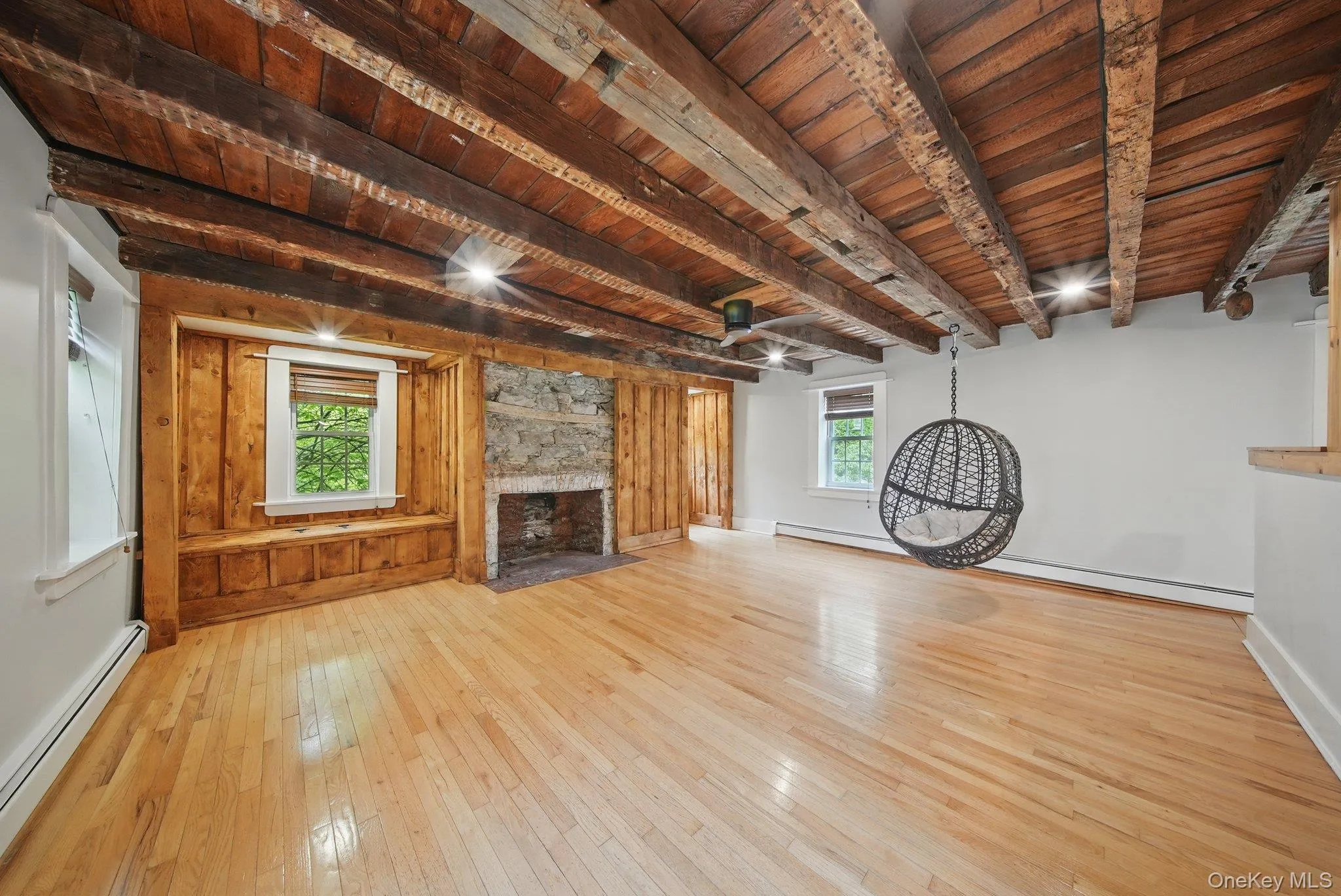 Unfurnished living room with a baseboard heating unit, a wooden ceiling with exposed beams, a fireplace, ceiling fan, and light wood-style flooring Unfurnished living room with a baseboard heating unit, a wooden ceiling with exposed beams, a fireplace, ceiling fan, and light wood-style flooring