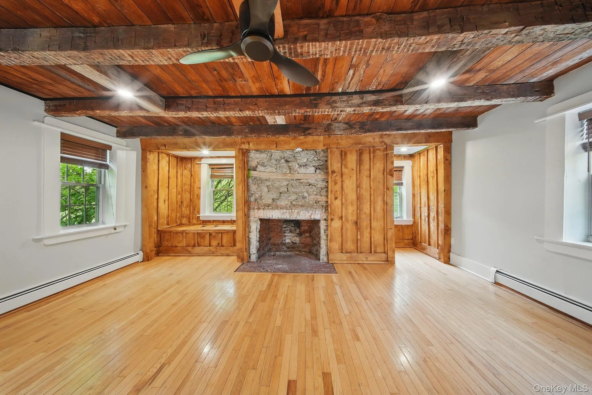 Unfurnished living room with a wooden ceiling with exposed beams, hardwood / wood-style floors, wood walls, a fireplace, and a ceiling fan Unfurnished living room with a wooden ceiling with exposed beams, hardwood / wood-style floors, wood walls, a fireplace, and a ceiling fan