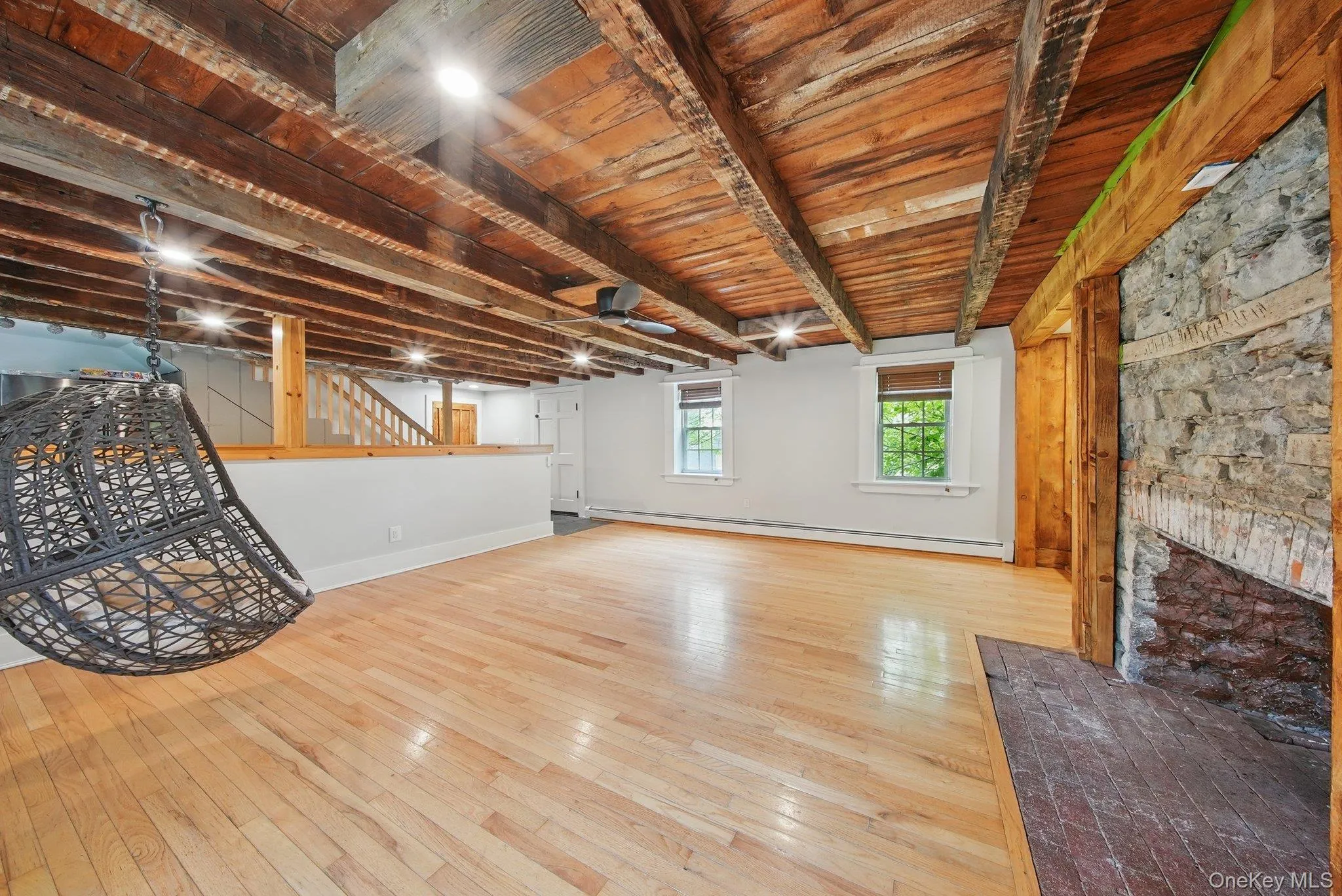 Unfurnished living room with a ceiling fan, light wood-style flooring, a baseboard heating unit, a wooden ceiling with exposed beams, and stairway Unfurnished living room with a ceiling fan, light wood-style flooring, a baseboard heating unit, a wooden ceiling with exposed beams, and stairway