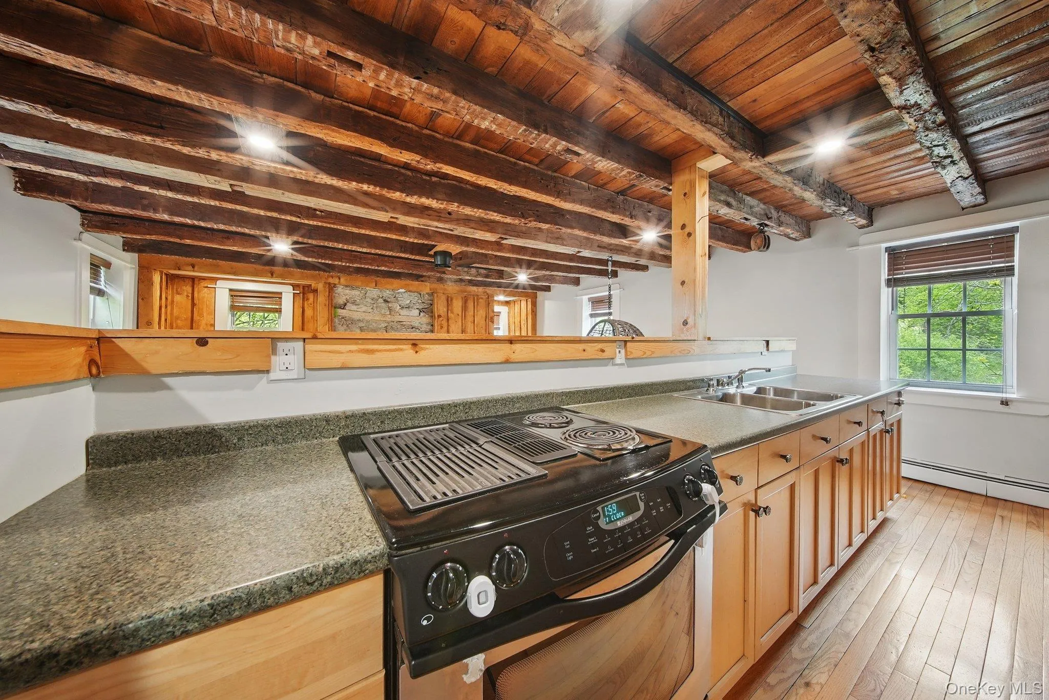 Kitchen with black / electric stove, a wooden ceiling with exposed beams, light wood-type flooring, and baseboard heating Kitchen with black / electric stove, a wooden ceiling with exposed beams, light wood-type flooring, and baseboard heating
