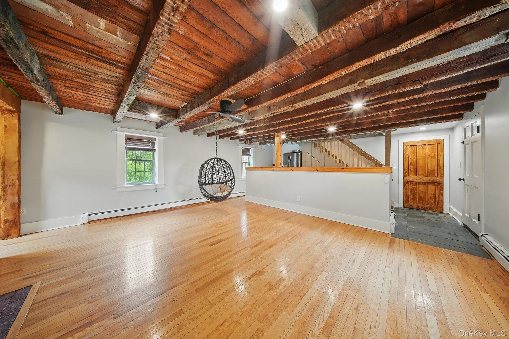 Unfurnished living room featuring stairs, light wood-style flooring, a wooden ceiling with exposed beams, and a baseboard heating unit Unfurnished living room featuring stairs, light wood-style flooring, a wooden ceiling with exposed beams, and a baseboard heating unit