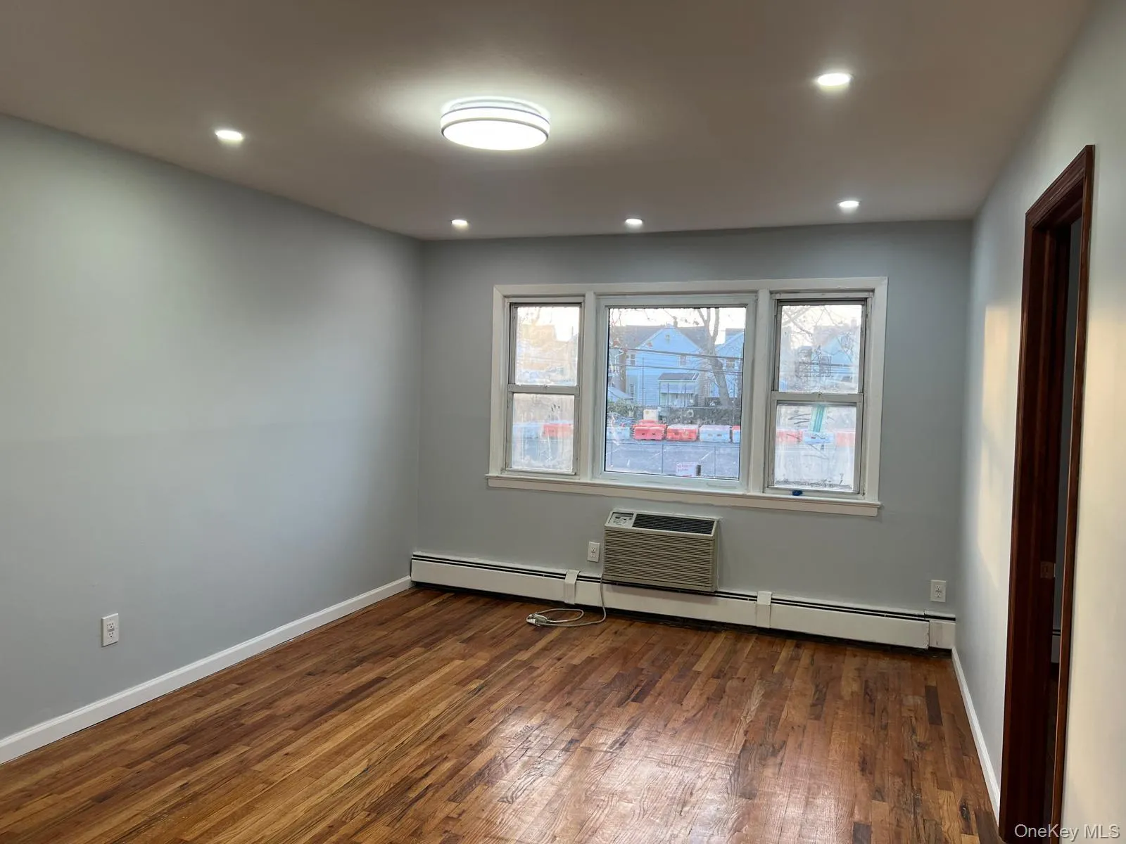 Unfurnished room with dark wood-style floors, a baseboard radiator, recessed lighting, and a wall mounted AC Unfurnished room with dark wood-style floors, a baseboard radiator, recessed lighting, and a wall mounted AC