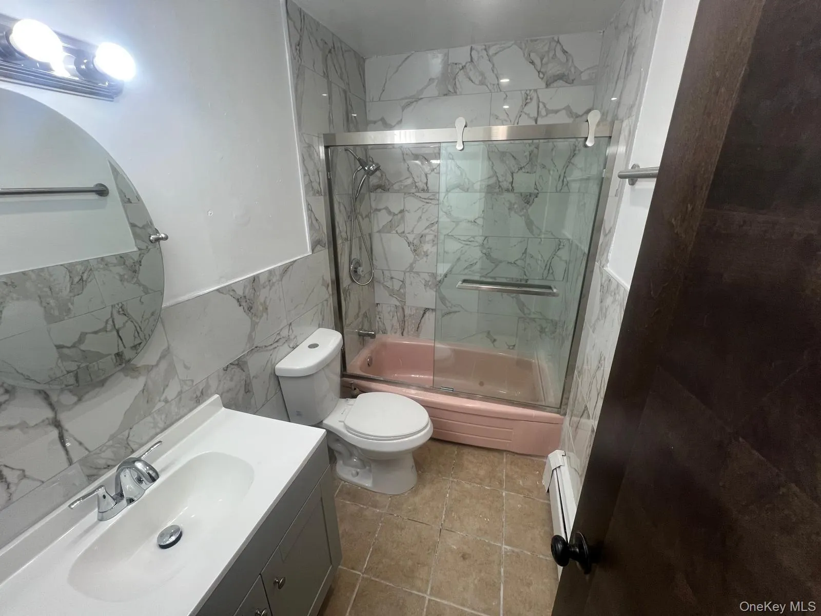 Full bath with tile walls, vanity, combined bath / shower with glass door, baseboard heating, and a wainscoted wall Full bath with tile walls, vanity, combined bath / shower with glass door, baseboard heating, and a wainscoted wall