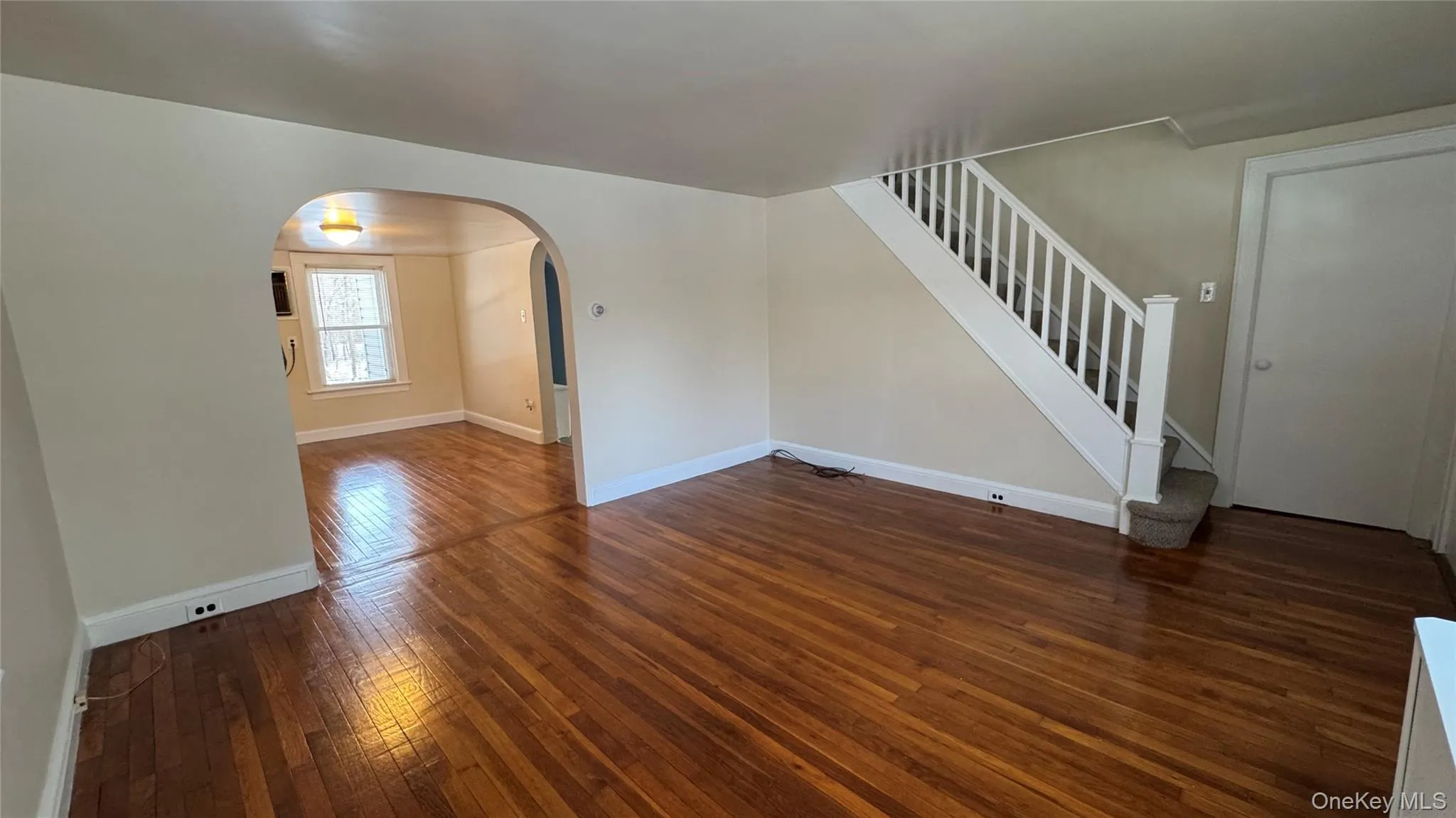 Unfurnished living room featuring dark wood-style flooring, arched walkways, and stairs Unfurnished living room featuring dark wood-style flooring, arched walkways, and stairs