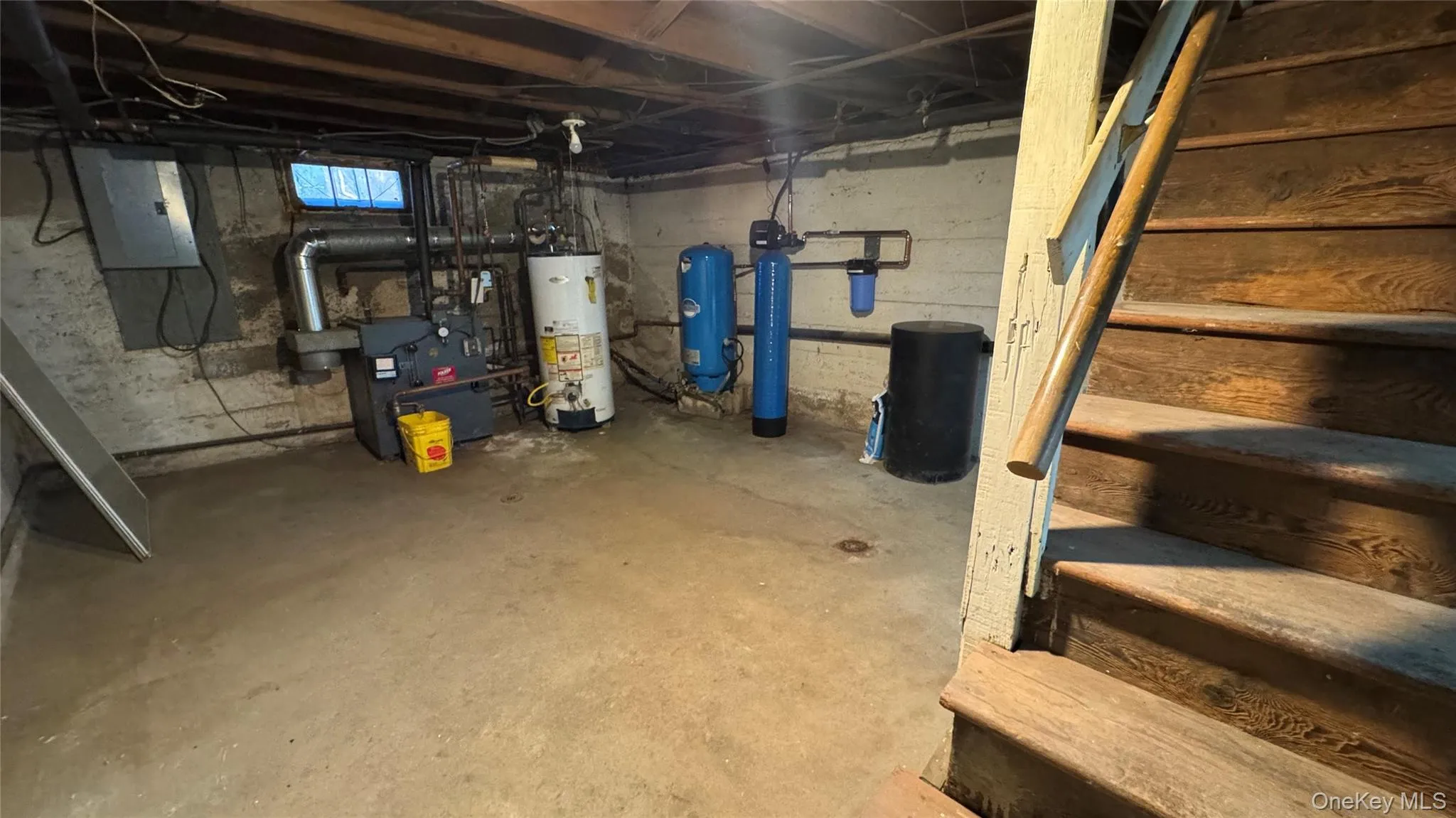 Unfinished basement with electric panel, water heater, a water softener, stairs, and a water pressure tank Unfinished basement with electric panel, water heater, a water softener, stairs, and a water pressure tank