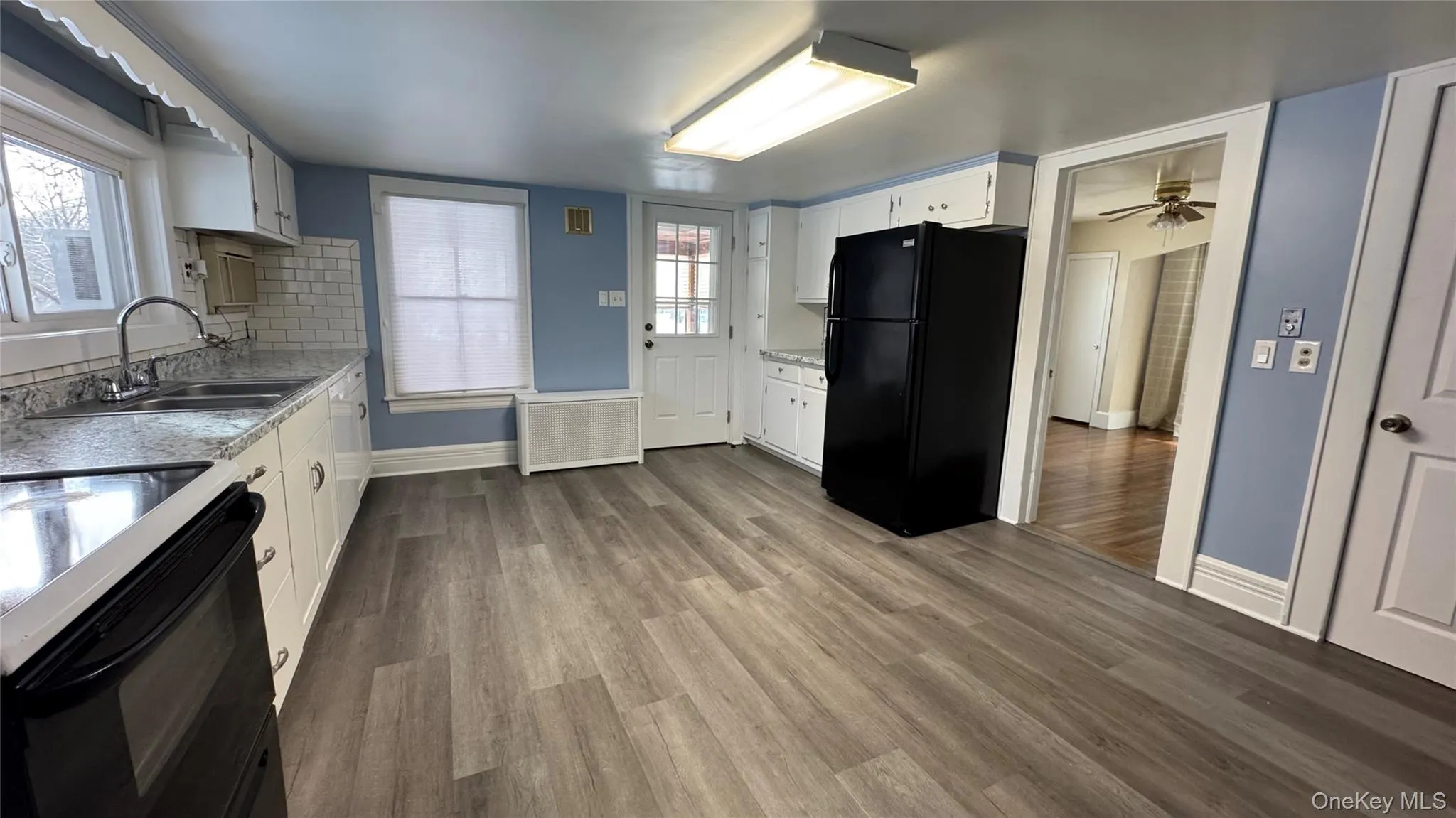 Kitchen with white cabinets, black appliances, dark wood-style flooring, radiator, and ceiling fan Kitchen with white cabinets, black appliances, dark wood-style flooring, radiator, and ceiling fan