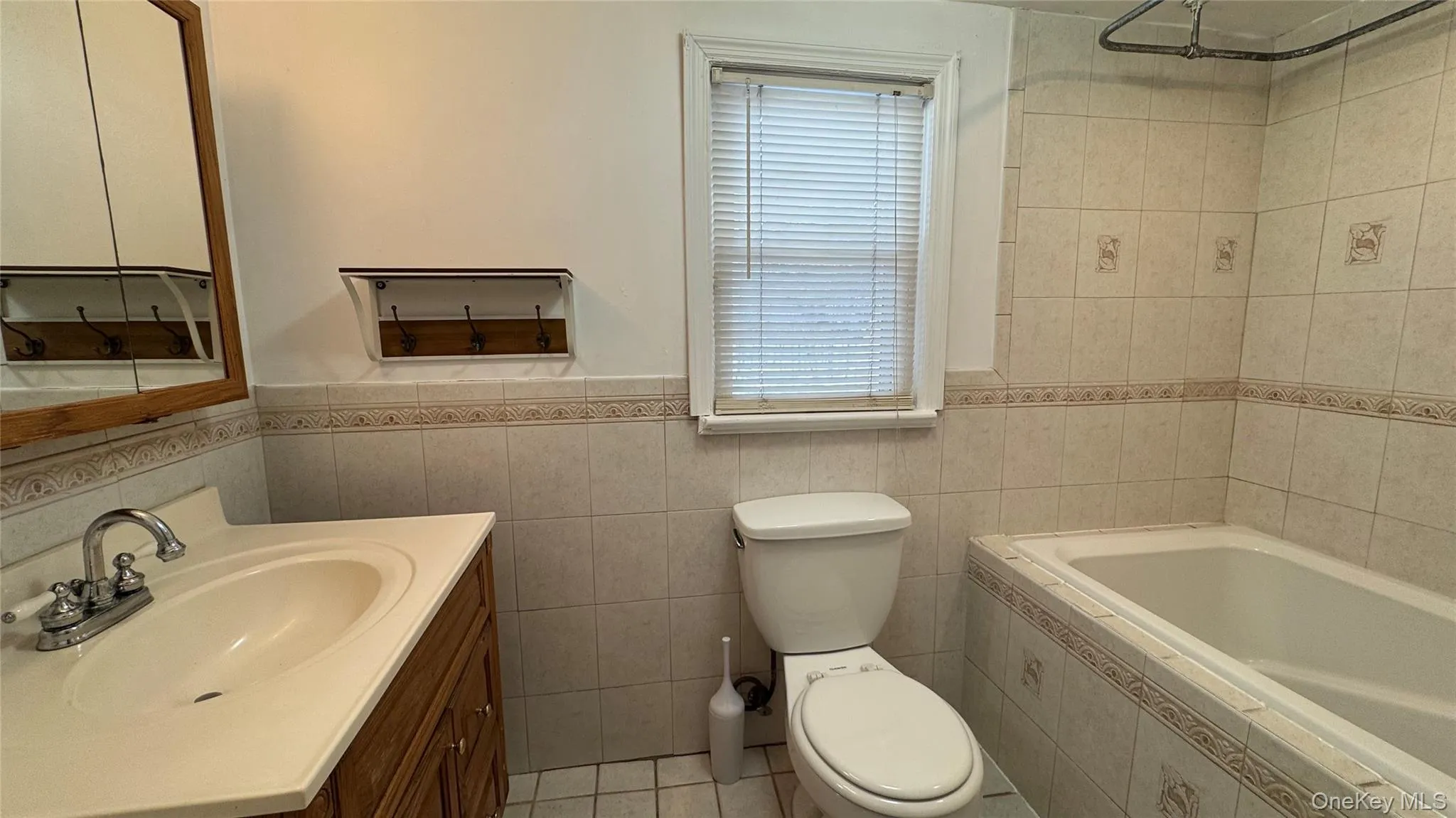 Bathroom with vanity, tile walls, a wainscoted wall, and light tile patterned floors Bathroom with vanity, tile walls, a wainscoted wall, and light tile patterned floors