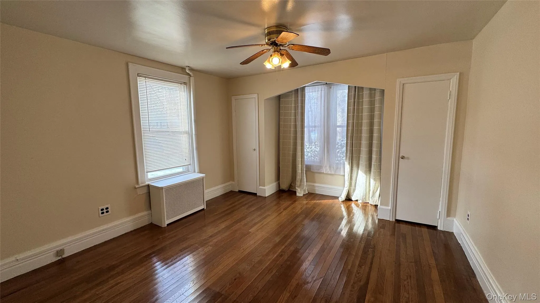 Empty room with dark wood-type flooring, radiator heating unit, and ceiling fan Empty room with dark wood-type flooring, radiator heating unit, and ceiling fan