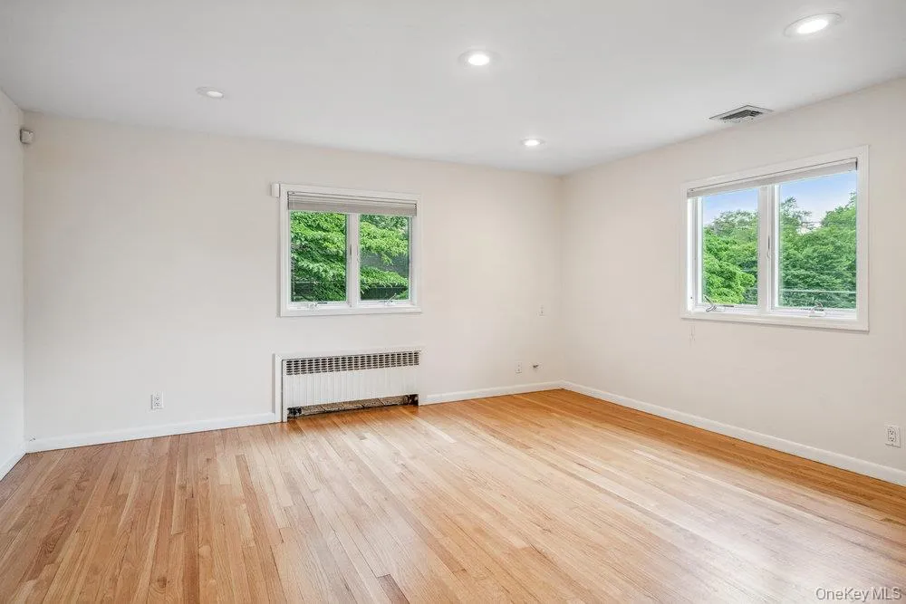 Empty room with radiator heating unit, light wood-type flooring, plenty of natural light, and recessed lighting Empty room with radiator heating unit, light wood-type flooring, plenty of natural light, and recessed lighting