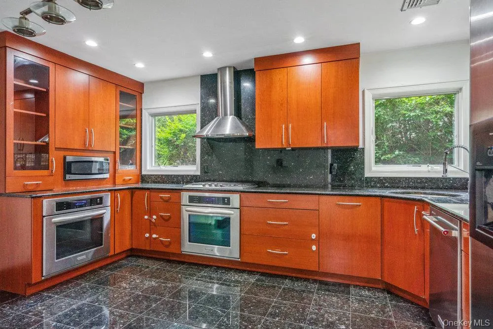 Kitchen with wall chimney range hood, appliances with stainless steel finishes, granite tiled floors, glass insert cabinets, and brown cabinets Kitchen with wall chimney range hood, appliances with stainless steel finishes, granite tiled floors, glass insert cabinets, and brown cabinets