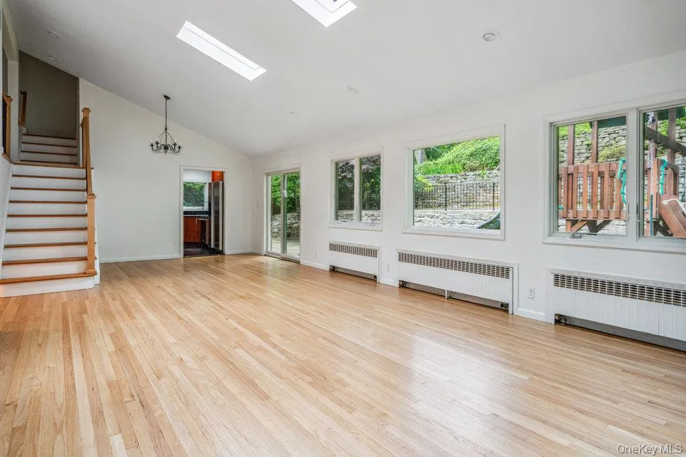 Unfurnished living room with a skylight, radiator heating unit, light wood-style floors, a chandelier, and high vaulted ceiling Unfurnished living room with a skylight, radiator heating unit, light wood-style floors, a chandelier, and high vaulted ceiling