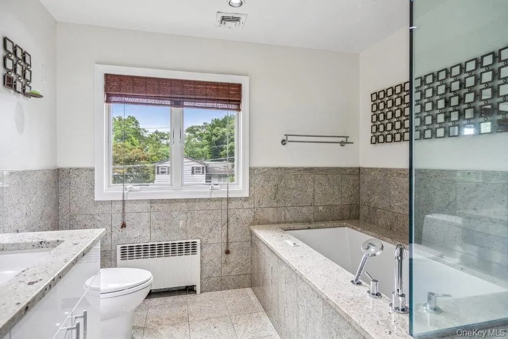 Full bath featuring radiator, a bath, vanity, and wainscoting Full bath featuring radiator, a bath, vanity, and wainscoting
