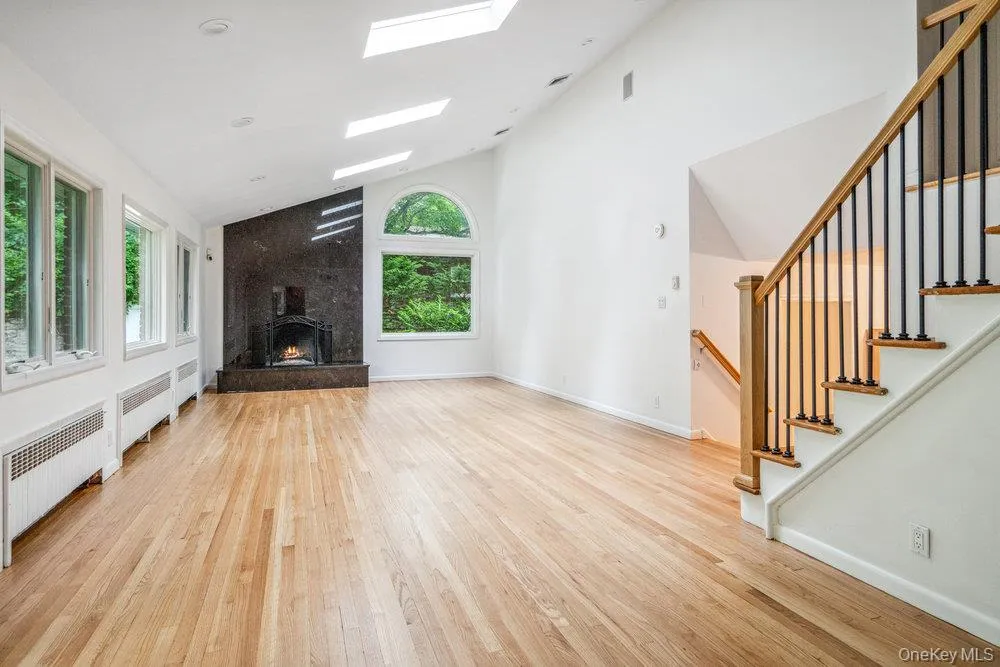 Unfurnished living room featuring light wood-style flooring, high vaulted ceiling, a skylight, healthy amount of natural light, and stairway Unfurnished living room featuring light wood-style flooring, high vaulted ceiling, a skylight, healthy amount of natural light, and stairway