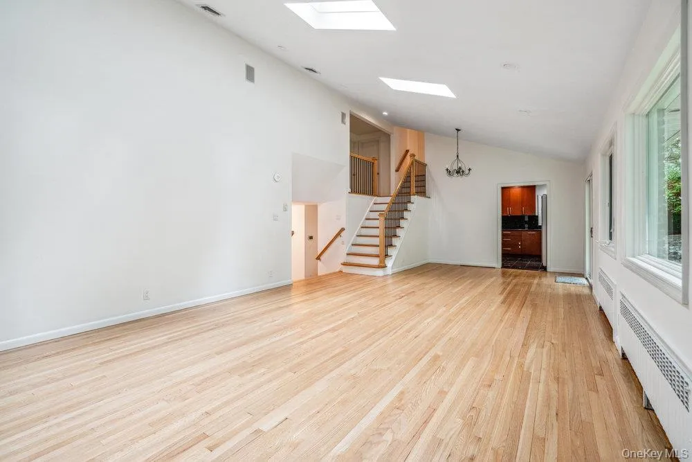 Unfurnished living room featuring light wood-style floors, a chandelier, a skylight, radiator heating unit, and stairway Unfurnished living room featuring light wood-style floors, a chandelier, a skylight, radiator heating unit, and stairway
