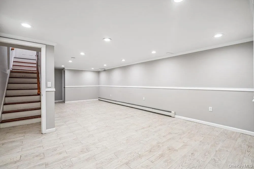 Finished basement with a baseboard radiator, stairs, light wood-style flooring, and recessed lighting Finished basement with a baseboard radiator, stairs, light wood-style flooring, and recessed lighting
