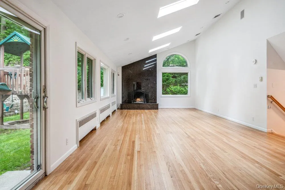 Unfurnished living room featuring radiator heating unit, light wood finished floors, high vaulted ceiling, a wood stove, and a skylight Unfurnished living room featuring radiator heating unit, light wood finished floors, high vaulted ceiling, a wood stove, and a skylight