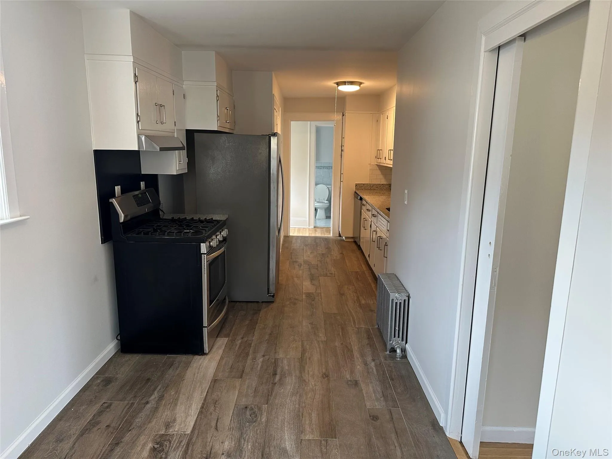 Kitchen featuring stainless steel range with gas stovetop, white cabinetry, dark wood finished floors, radiator, and under cabinet range hood Kitchen featuring stainless steel range with gas stovetop, white cabinetry, dark wood finished floors, radiator, and under cabinet range hood