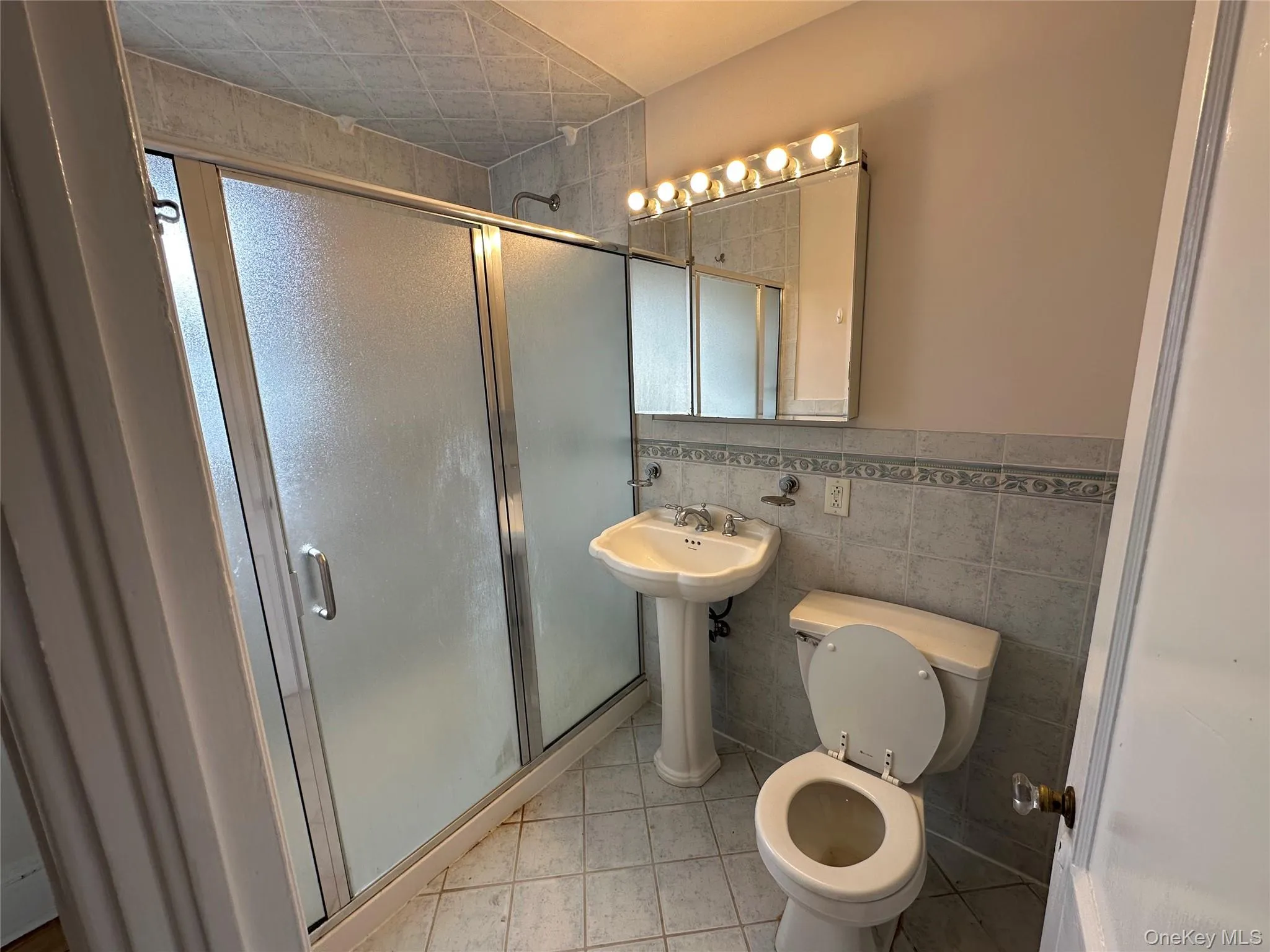 Bathroom featuring a stall shower, tile walls, a wainscoted wall, and light tile patterned floors Bathroom featuring a stall shower, tile walls, a wainscoted wall, and light tile patterned floors