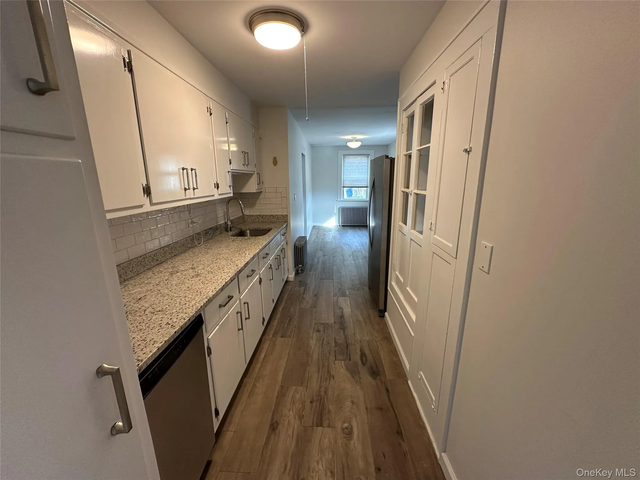 Kitchen featuring light stone counters, white cabinetry, appliances with stainless steel finishes, dark wood-style flooring, and tasteful backsplash Kitchen featuring light stone counters, white cabinetry, appliances with stainless steel finishes, dark wood-style flooring, and tasteful backsplash