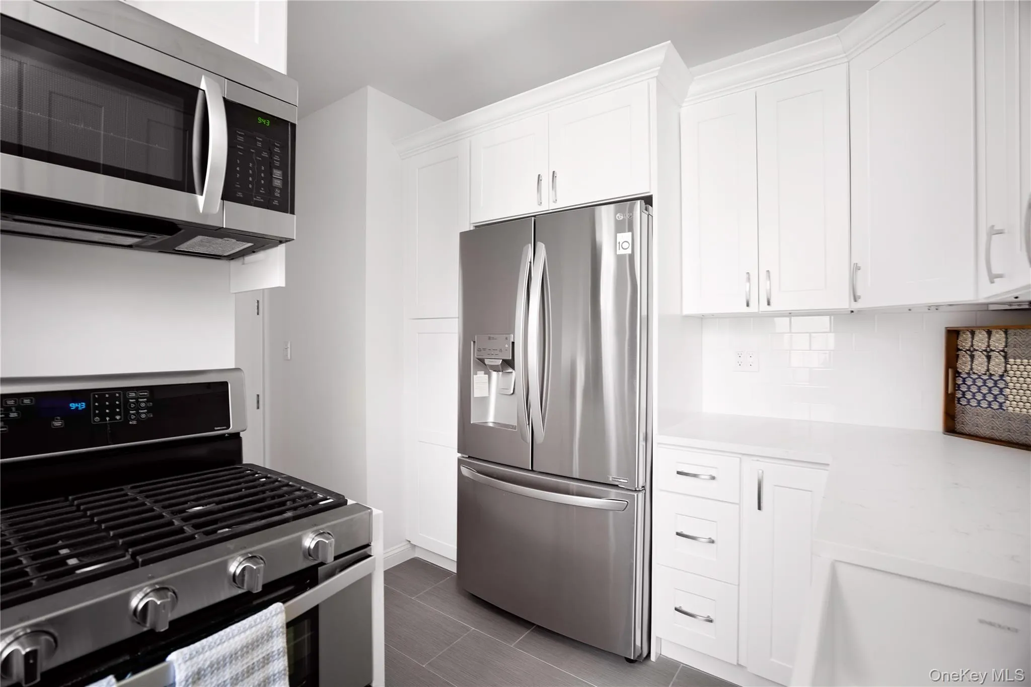 Kitchen with appliances with stainless steel finishes, white cabinetry, tasteful backsplash, and light stone countertops Kitchen with appliances with stainless steel finishes, white cabinetry, tasteful backsplash, and light stone countertops