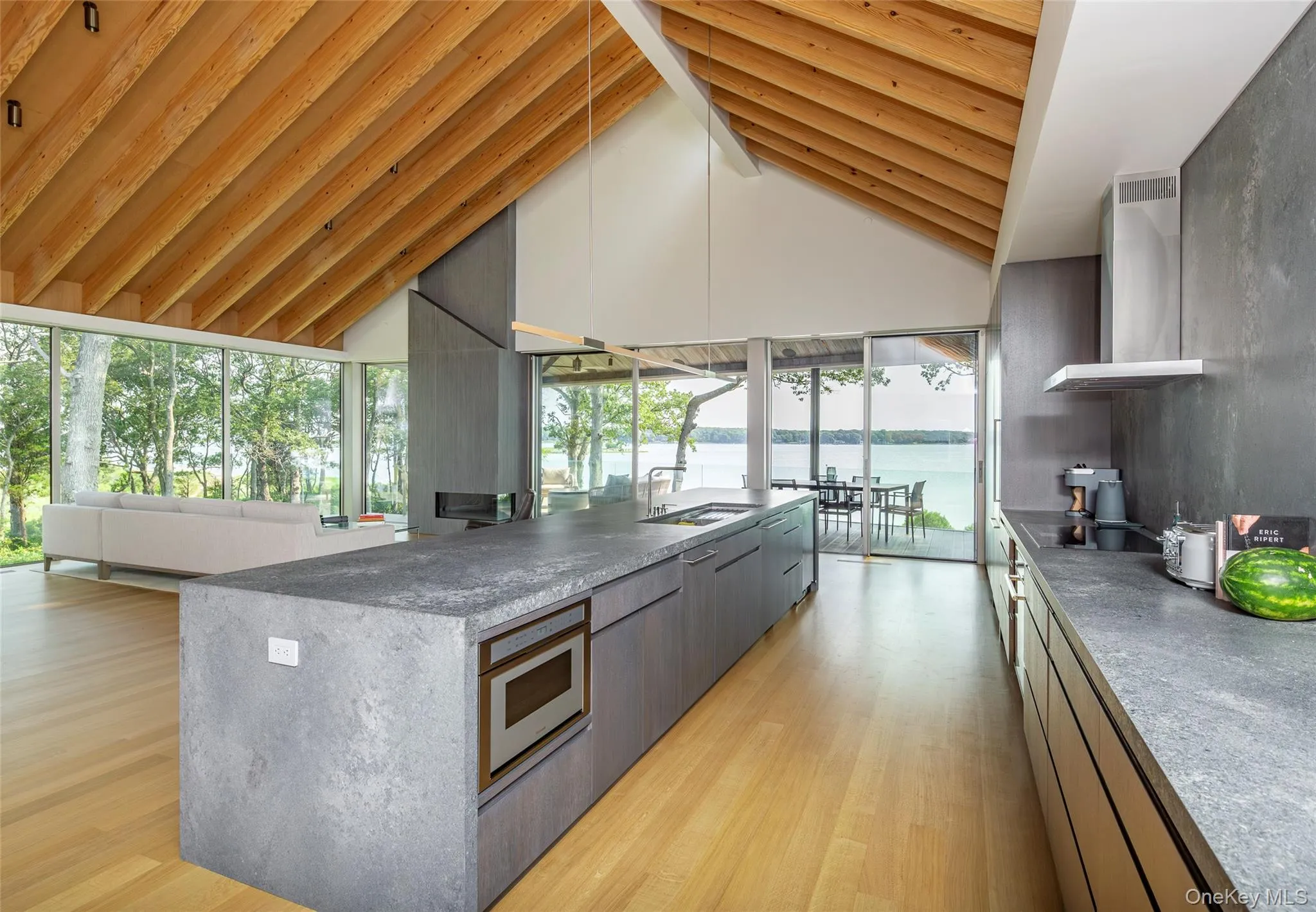 Kitchen featuring wall chimney range hood, light wood-style floors, a water view, modern cabinets, and open floor plan Kitchen featuring wall chimney range hood, light wood-style floors, a water view, modern cabinets, and open floor plan