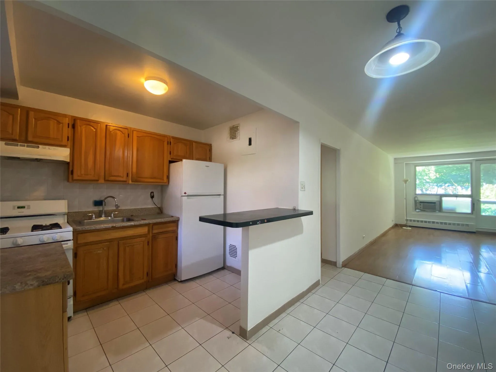 Kitchen featuring brown cabinetry, white appliances, decorative backsplash, dark countertops, and under cabinet range hood Kitchen featuring brown cabinetry, white appliances, decorative backsplash, dark countertops, and under cabinet range hood