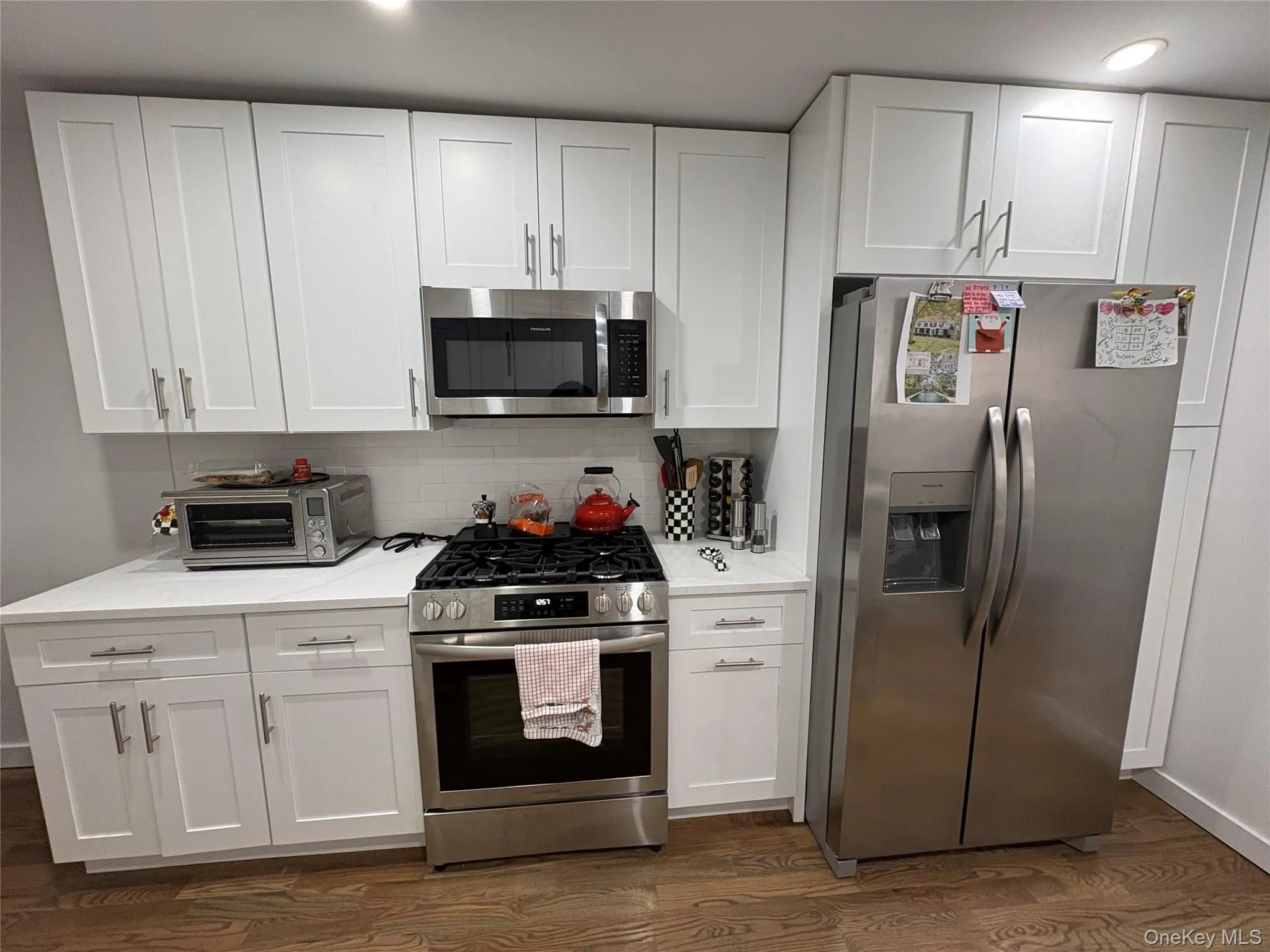 Kitchen with stainless steel appliances, white cabinets, dark wood-style floors, and tasteful backsplash Kitchen with stainless steel appliances, white cabinets, dark wood-style floors, and tasteful backsplash