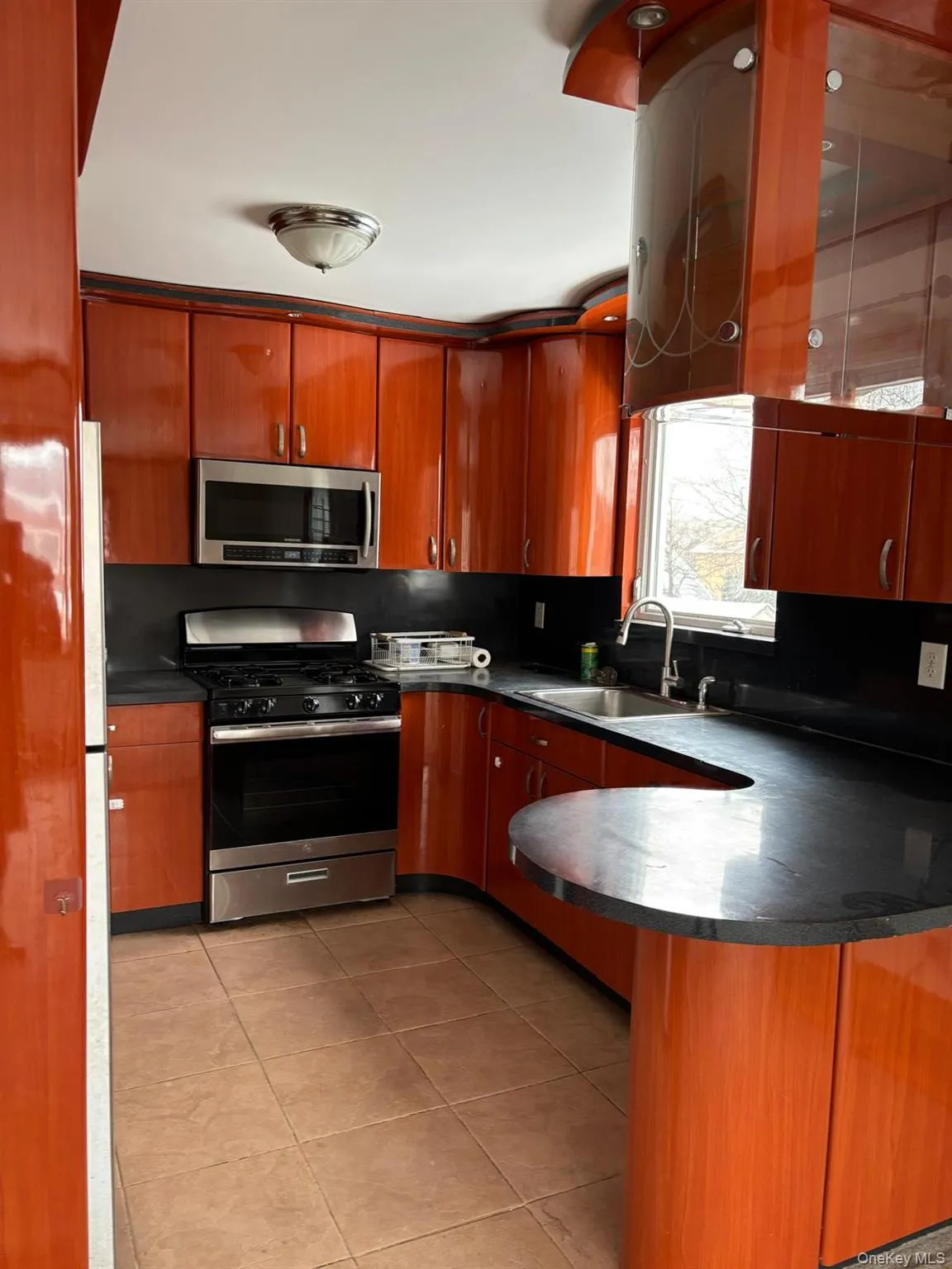 Kitchen with appliances with stainless steel finishes, light tile patterned floors, dark countertops, a peninsula, and tasteful backsplash Kitchen with appliances with stainless steel finishes, light tile patterned floors, dark countertops, a peninsula, and tasteful backsplash