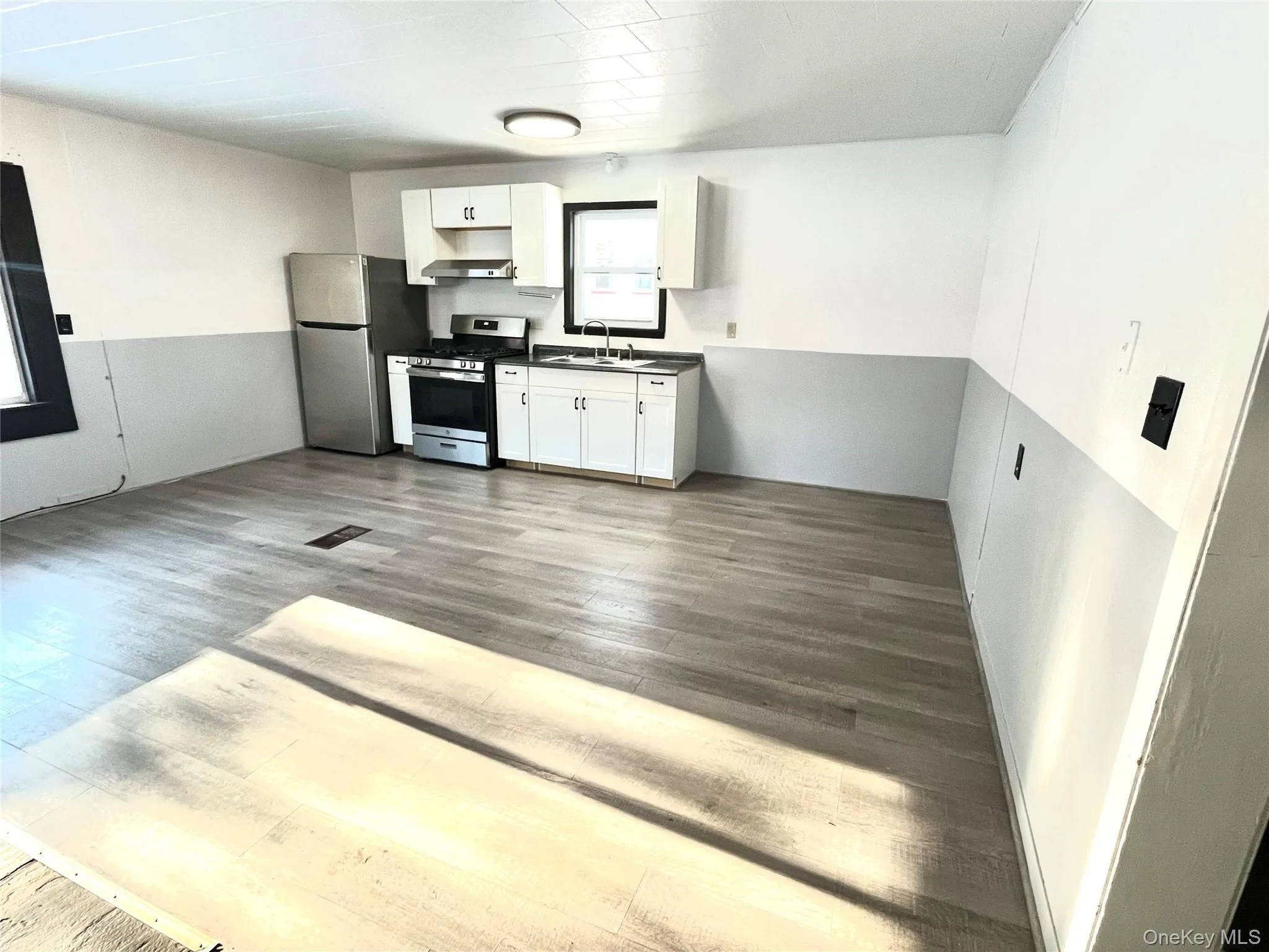 Kitchen featuring white cabinets, stainless steel appliances, dark countertops, dark wood-style flooring, and under cabinet range hood Kitchen featuring white cabinets, stainless steel appliances, dark countertops, dark wood-style flooring, and under cabinet range hood