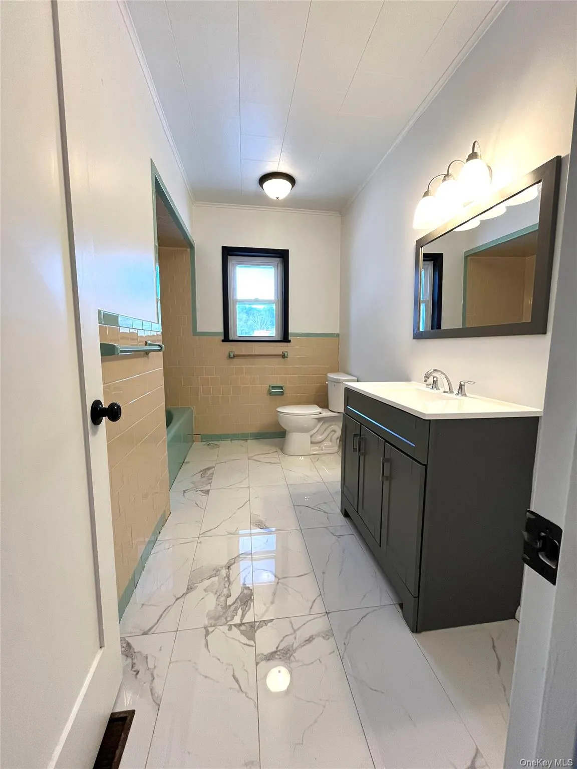 Bathroom with wainscoting, vanity, a tub to relax in, crown molding, and light marble finish flooring Bathroom with wainscoting, vanity, a tub to relax in, crown molding, and light marble finish flooring