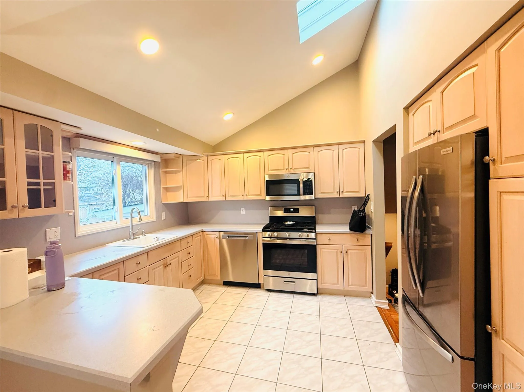 Kitchen with appliances with stainless steel finishes, light countertops, a skylight, open shelves, and glass insert cabinets Kitchen with appliances with stainless steel finishes, light countertops, a skylight, open shelves, and glass insert cabinets