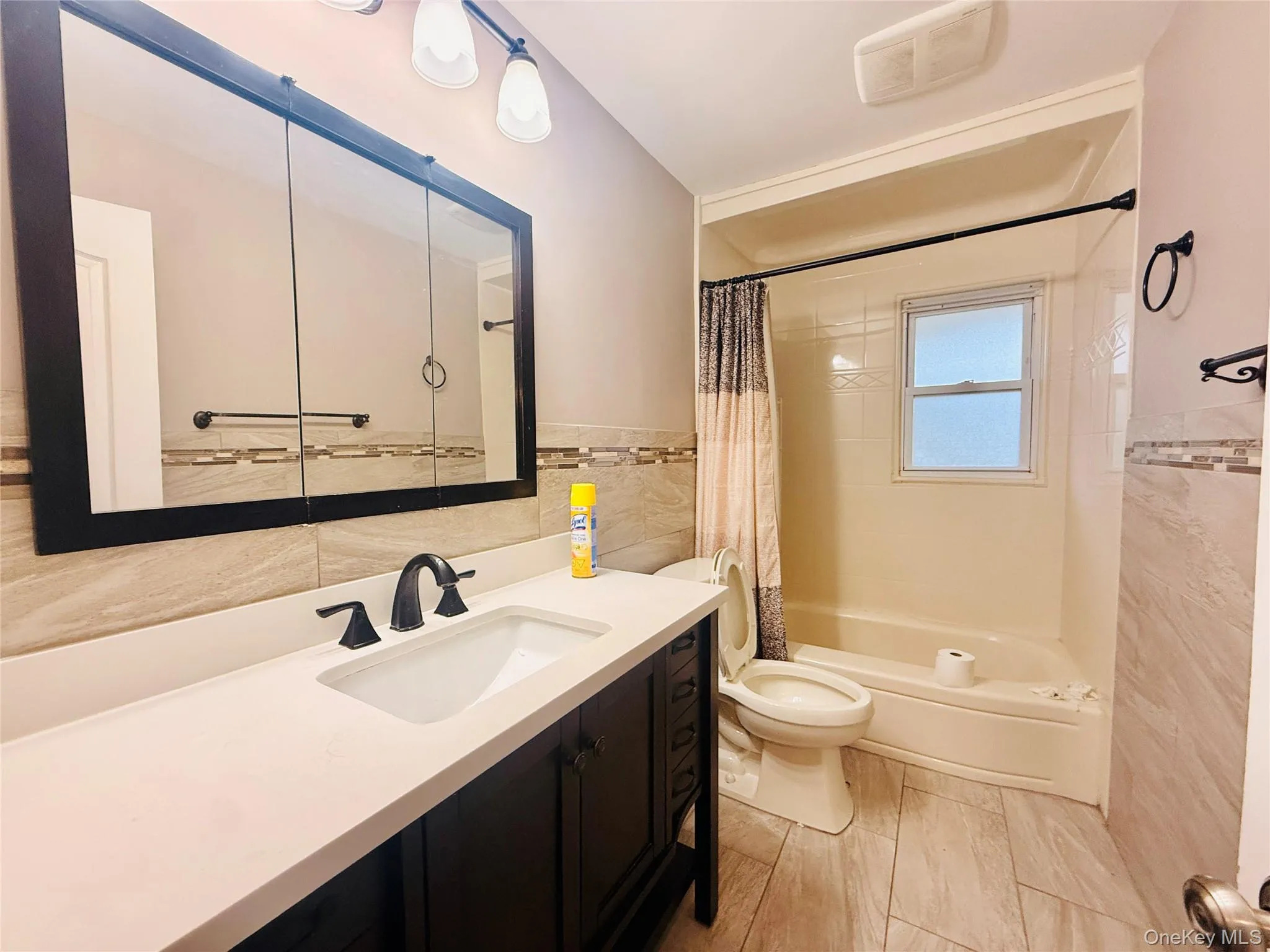 Full bath featuring tile walls, vanity, shower / bath combination with curtain, and wainscoting Full bath featuring tile walls, vanity, shower / bath combination with curtain, and wainscoting