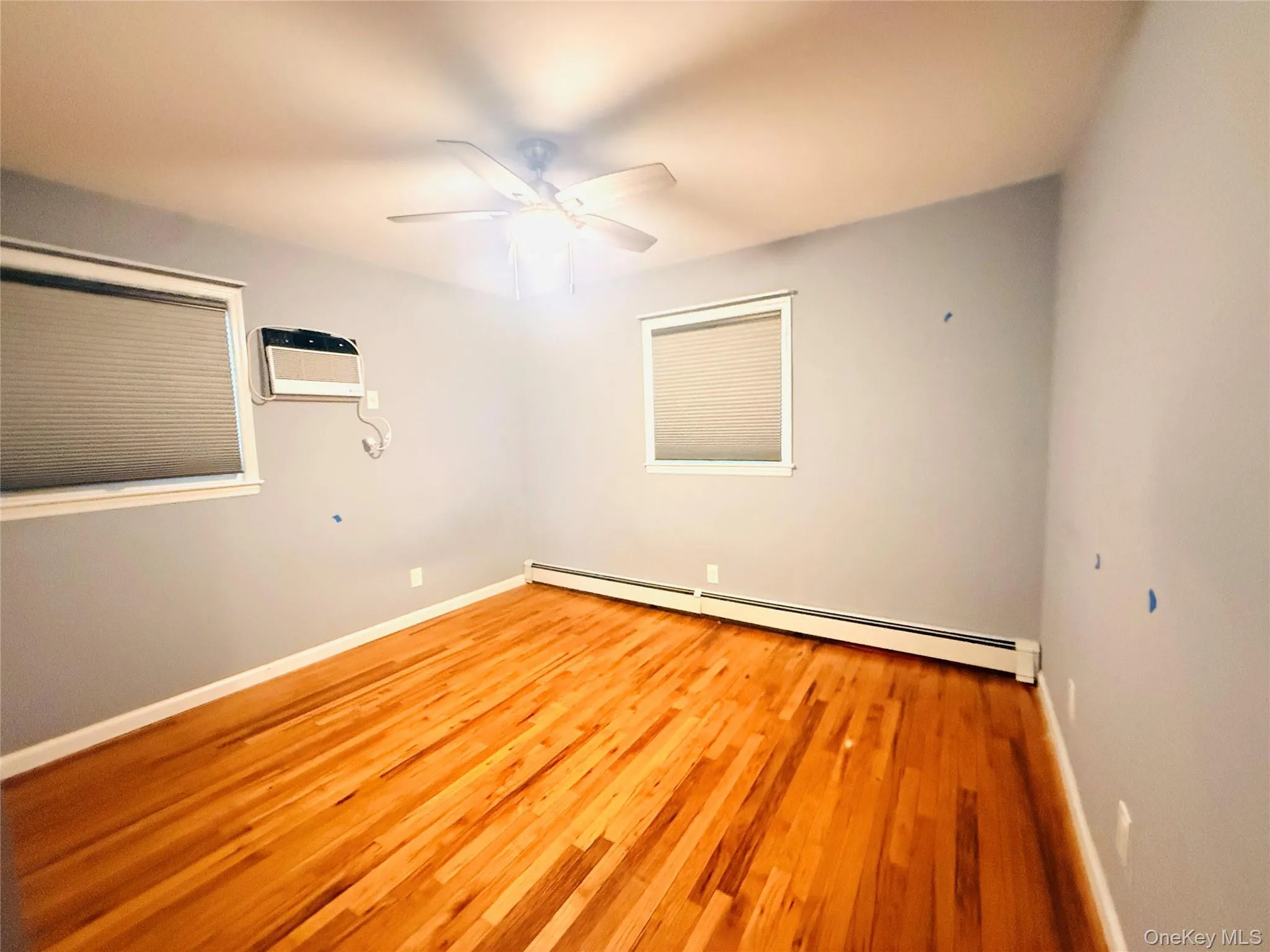 Unfurnished room with a baseboard heating unit, light wood-type flooring, ceiling fan, and an AC wall unit Unfurnished room with a baseboard heating unit, light wood-type flooring, ceiling fan, and an AC wall unit