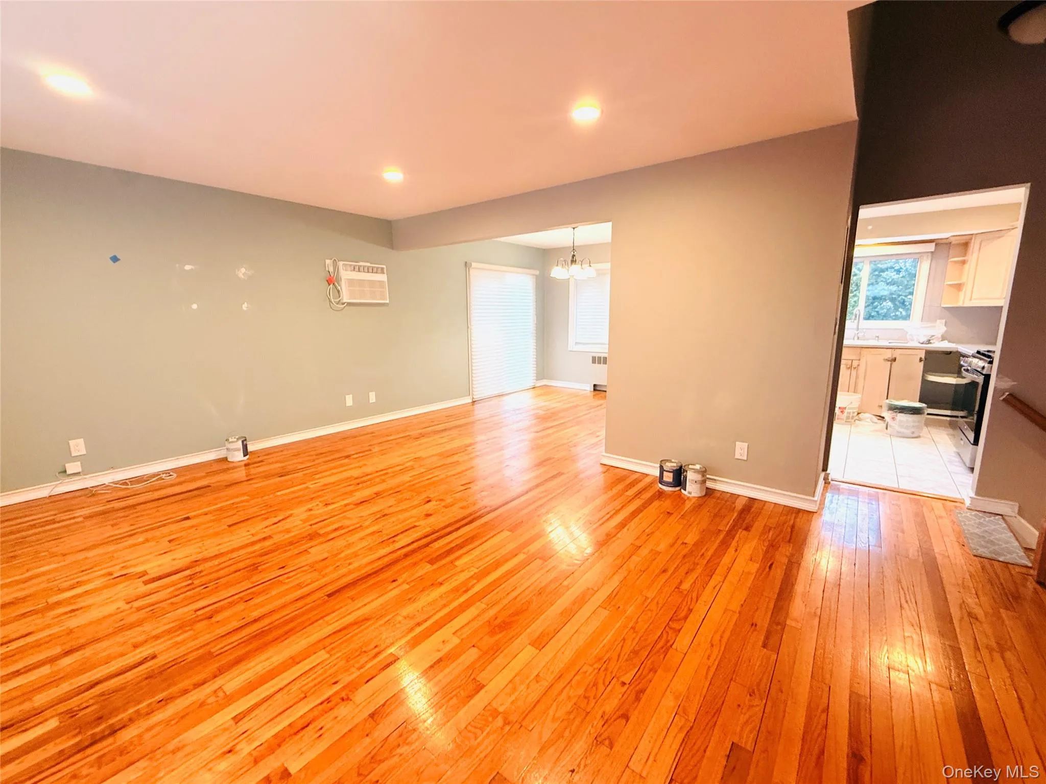 Unfurnished living room with a chandelier, light wood finished floors, recessed lighting, radiator heating unit, and a wall mounted AC Unfurnished living room with a chandelier, light wood finished floors, recessed lighting, radiator heating unit, and a wall mounted AC