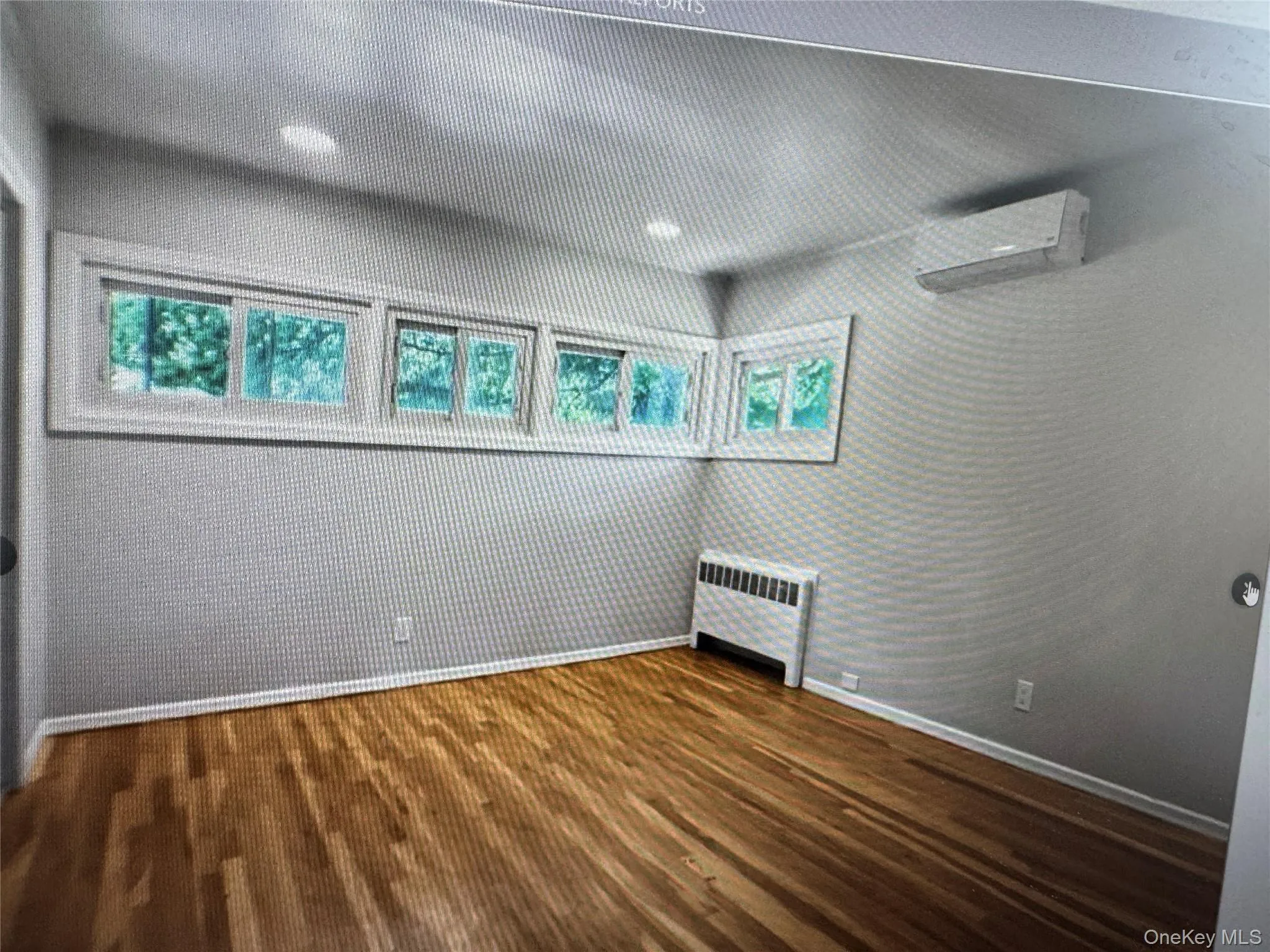 Empty room with dark wood-style floors, a wall mounted AC, and radiator Empty room with dark wood-style floors, a wall mounted AC, and radiator