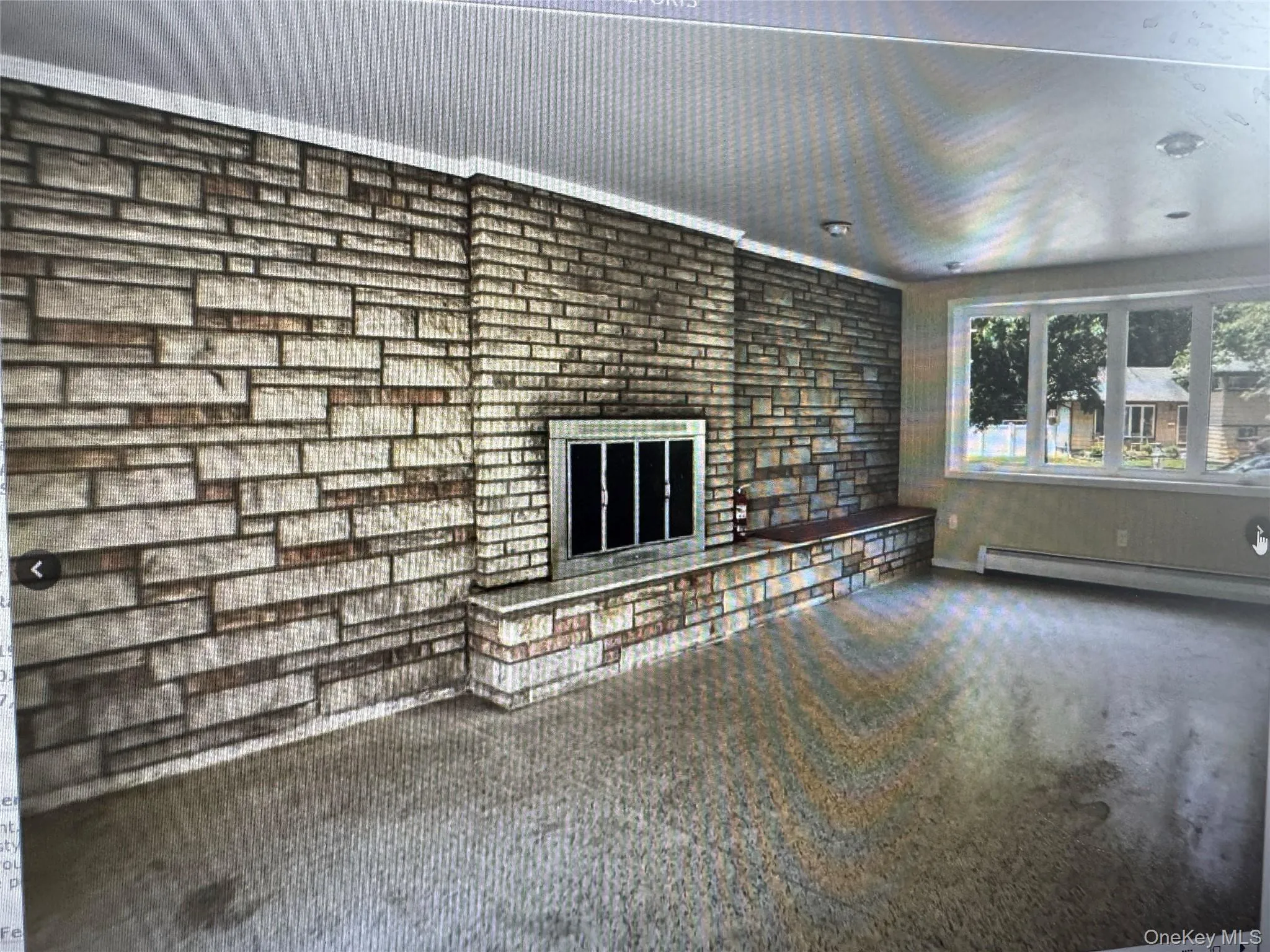 Unfurnished living room featuring carpet, a brick fireplace, and a baseboard heating unit Unfurnished living room featuring carpet, a brick fireplace, and a baseboard heating unit