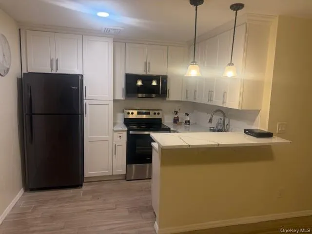 Kitchen featuring stainless steel appliances, a peninsula, white cabinetry, pendant lighting, and light wood finished floors Kitchen featuring stainless steel appliances, a peninsula, white cabinetry, pendant lighting, and light wood finished floors