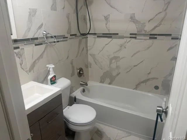 Full bathroom featuring vanity, shower / bath combination, marble look tiles, and tile walls Full bathroom featuring vanity, shower / bath combination, marble look tiles, and tile walls