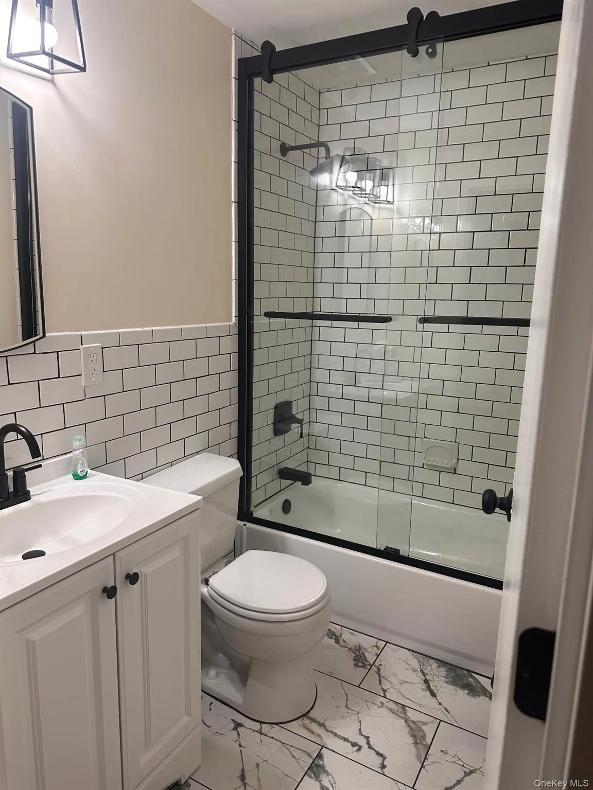 Bathroom with combined bath / shower with glass door, vanity, tile walls, and light marble finish floors Bathroom with combined bath / shower with glass door, vanity, tile walls, and light marble finish floors