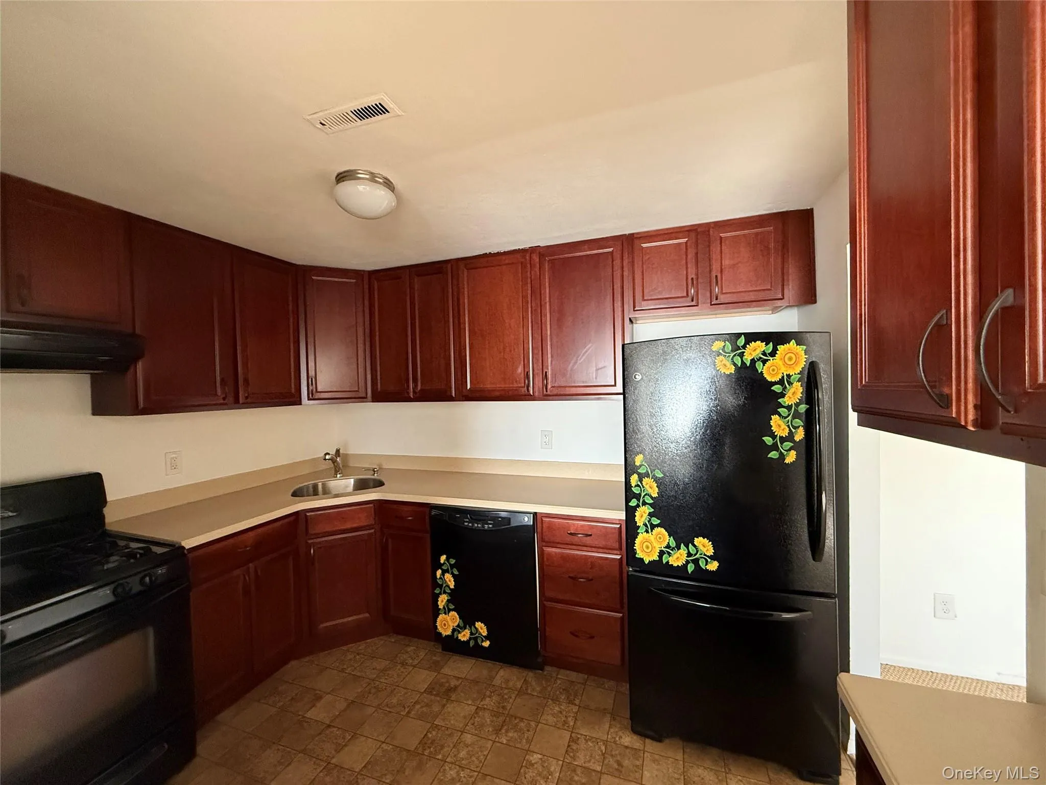 Kitchen with black appliances, light countertops, ventilation hood, dark brown cabinets, and stone finish flooring Kitchen with black appliances, light countertops, ventilation hood, dark brown cabinets, and stone finish flooring