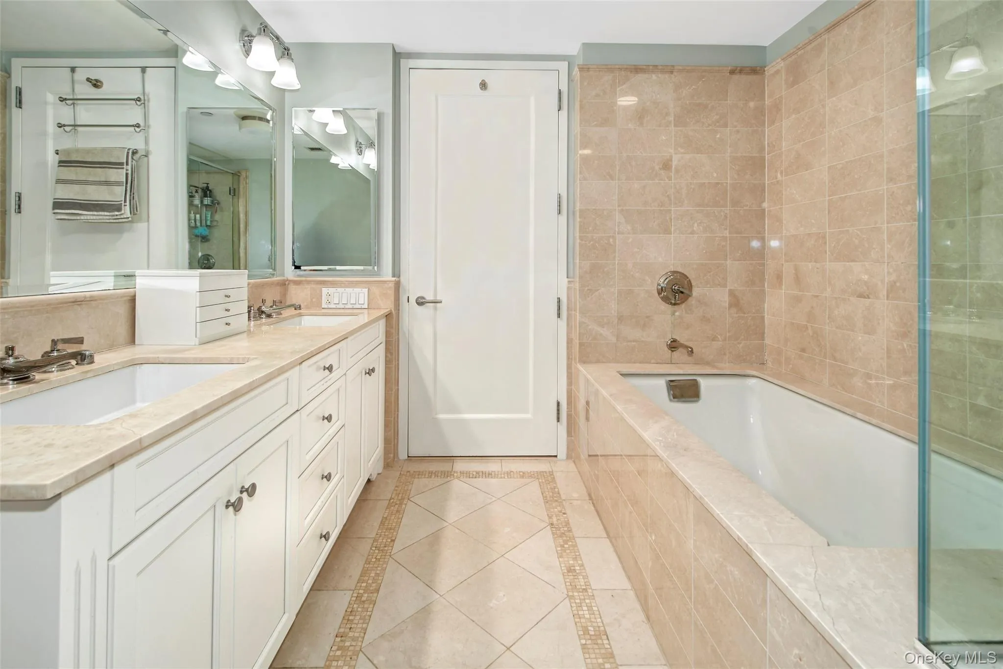 Bathroom featuring inlaid floor details, double vanity, a stall shower, tiled bath, and tile walls Bathroom featuring inlaid floor details, double vanity, a stall shower, tiled bath, and tile walls